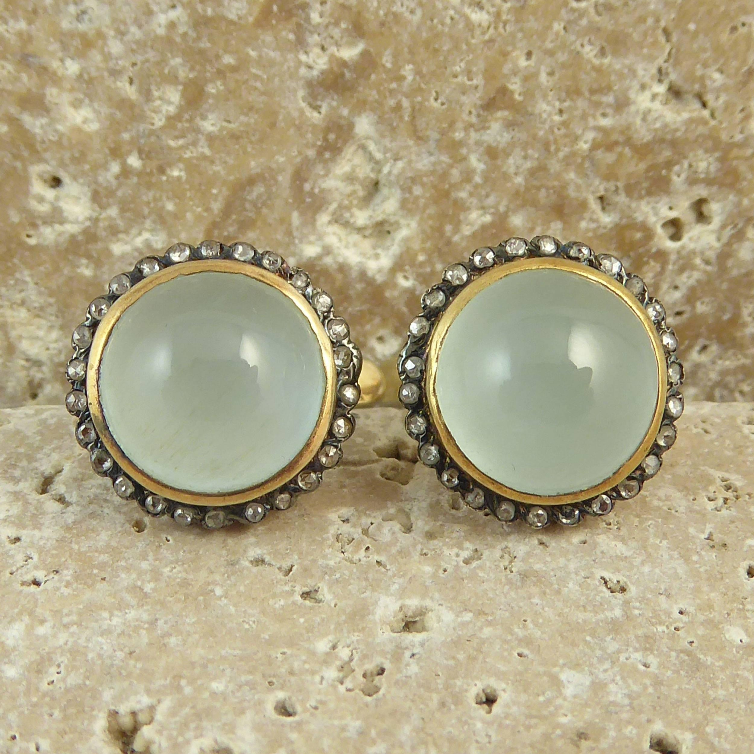 A pair of stone set stud earrings each comprising a central, rub-over set cabochon cut aquamarine of pale blue colour and showing chatoyancy.  Each aquamarine measures approx. 0.43 inch diameter x .24 inch deep and are set within a white bezel mount