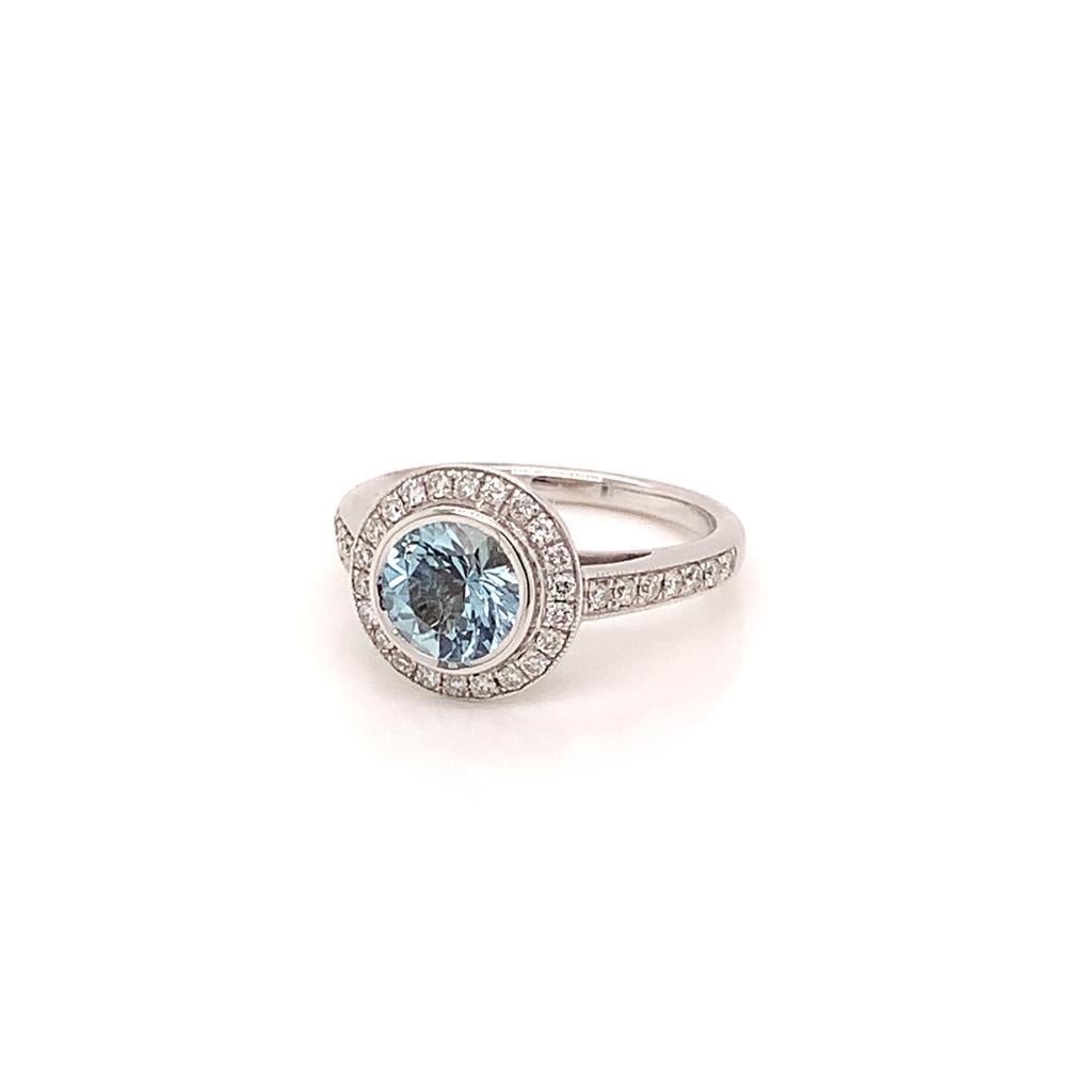 At the centre of this Gorgeous ring is a Lustrous Round Aquamarine weighing approximately 1.10 Carats which is surrounded by glittering Round Brilliant Diamonds in a halo setting that extend to the 18K White Gold band of this ring. The diamonds