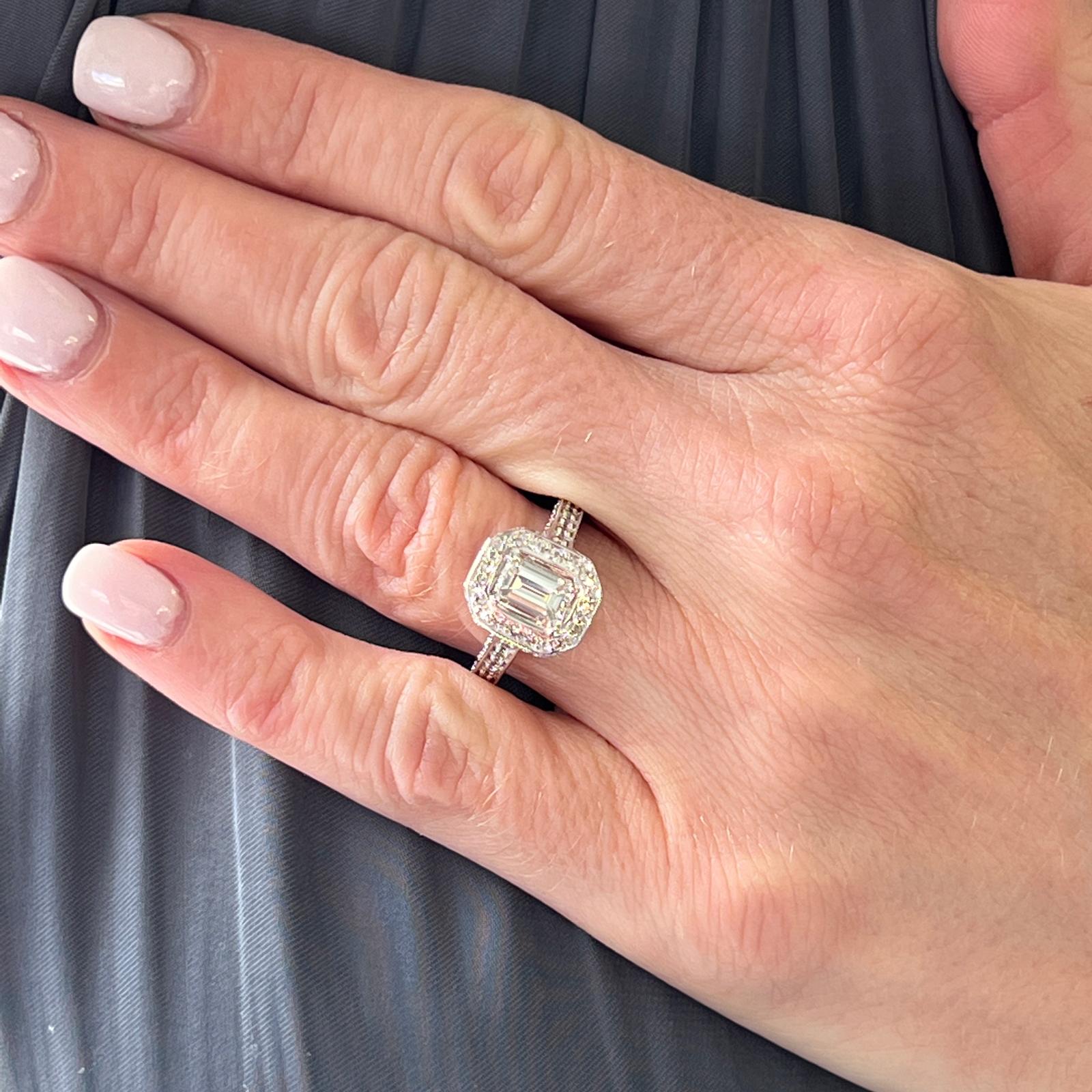 Gorgeous emerald cut diamond halo engagement ring fashioned in  14 karat white gold. The ring features an 1.10 carat emerald cut diamond graded by the GIA I color and VS1 clarity. The diamond is set in a modern halo mounting featuring approximately