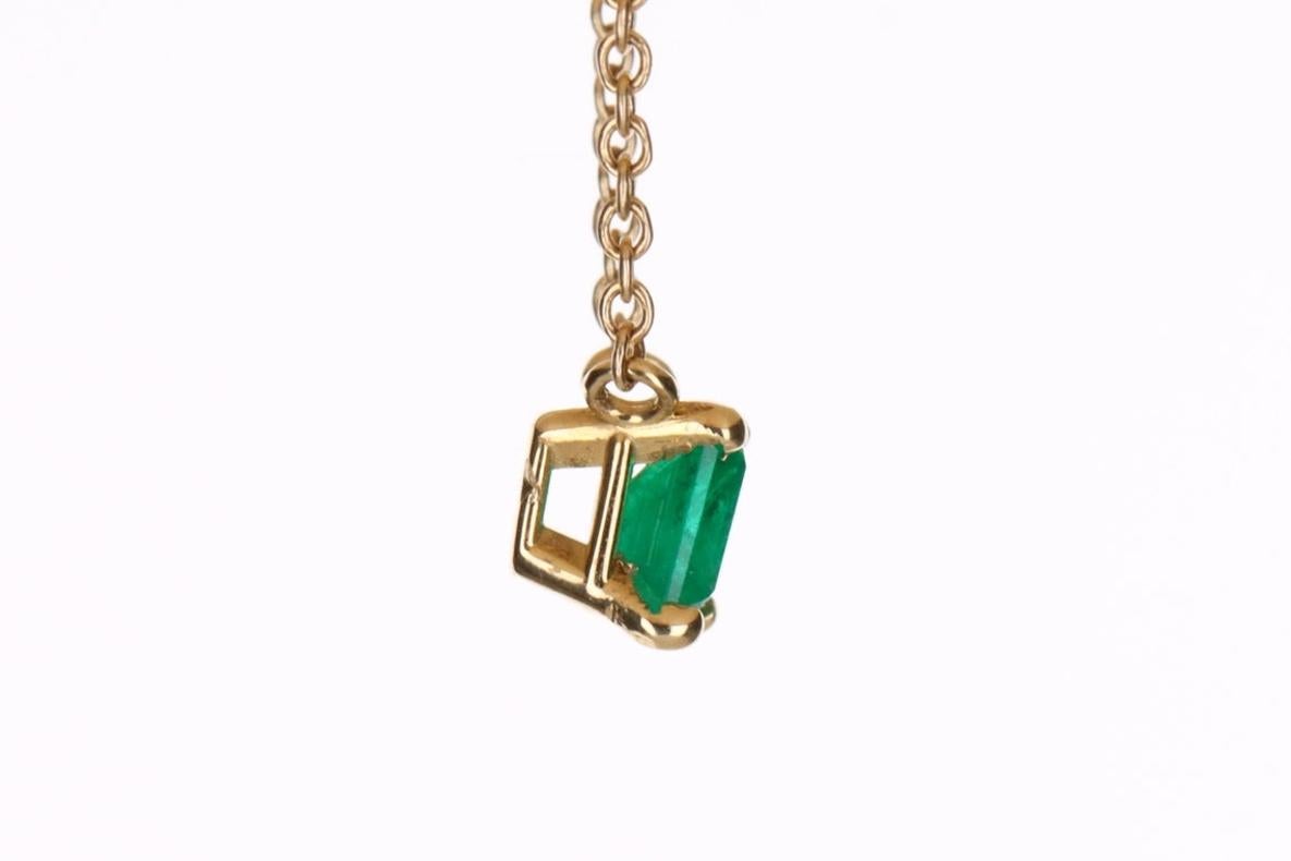 Displayed is an East to West Colombian emerald solitaire necklace. This gorgeous solitaire ring carries an emerald-cut emerald in a four-prong setting. Fully faceted, this gemstone showcases excellent shine. The emerald has excellent clarity with