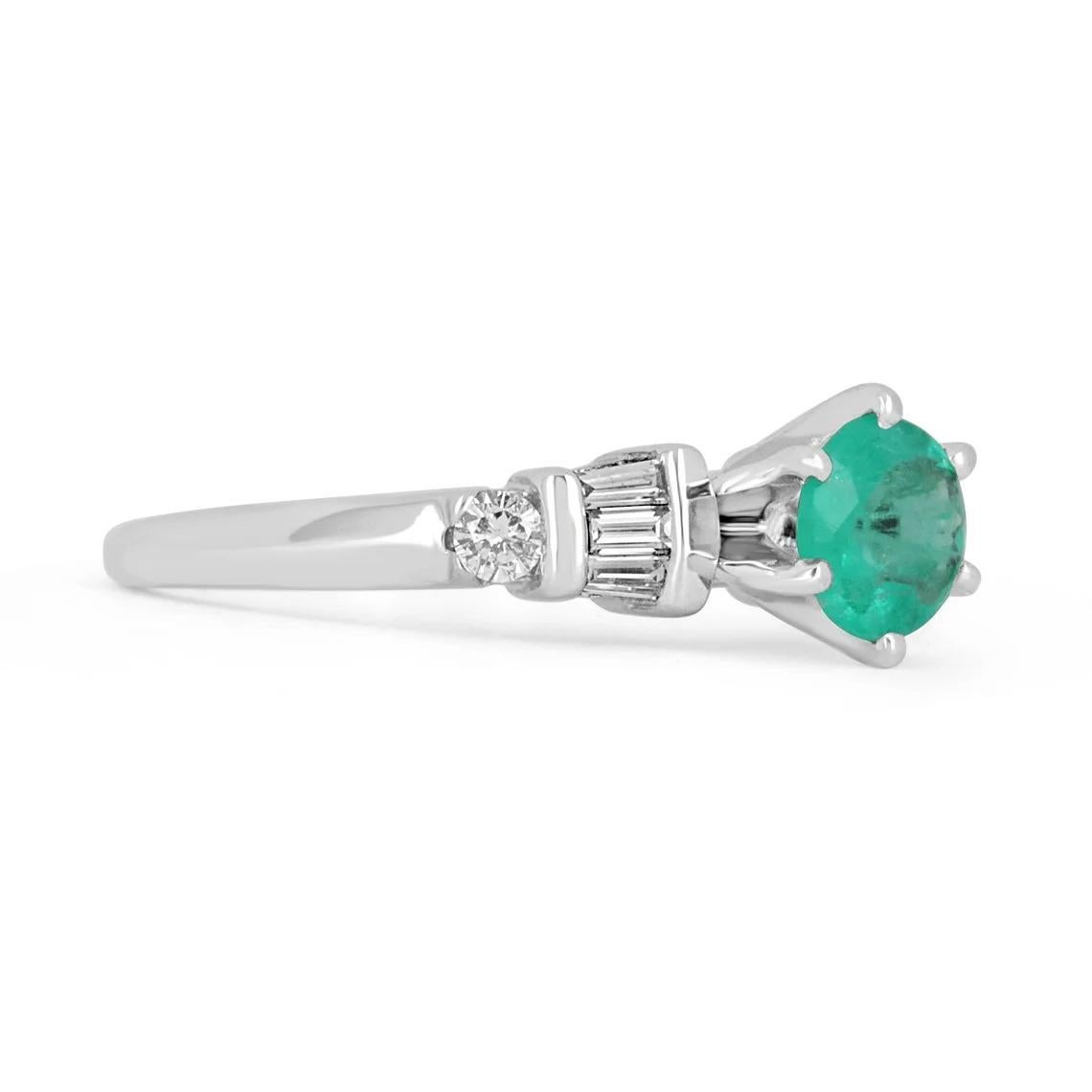 Displayed is a stunning emerald and diamond ring. The center gemstone is a round-cut emerald handset in a six-prong setting that allows for a full view of the emerald. Tapered baguette and brilliant round diamonds are tension set on the shank of the