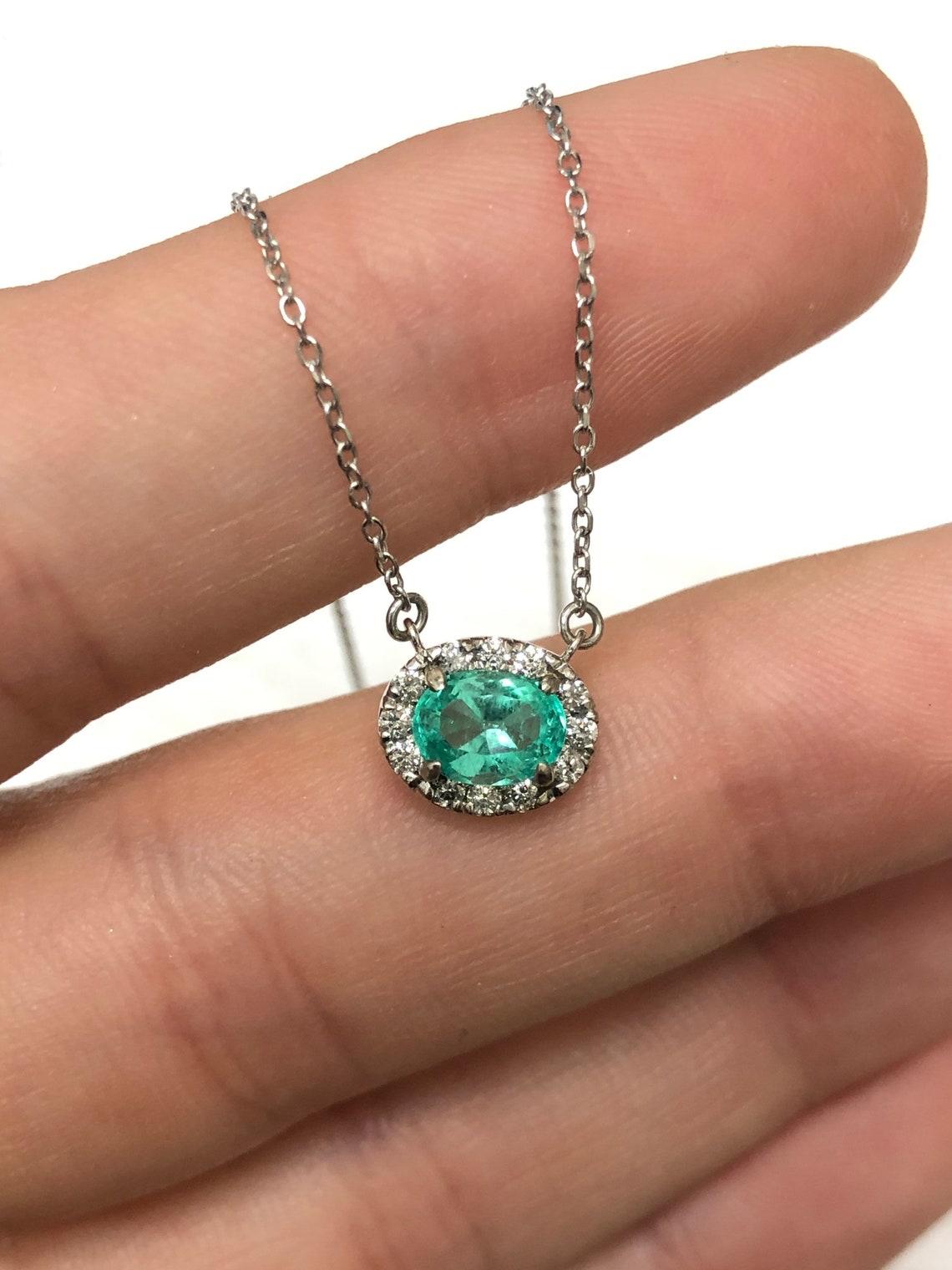 Featured here is a stunning oval Colombian emerald and diamond pendant made in fine 14K white gold. Displayed is a lustrous, bluish-green emerald with incredible transparency, accented by a simple four-prong 14K mount, allowing for the emerald to be