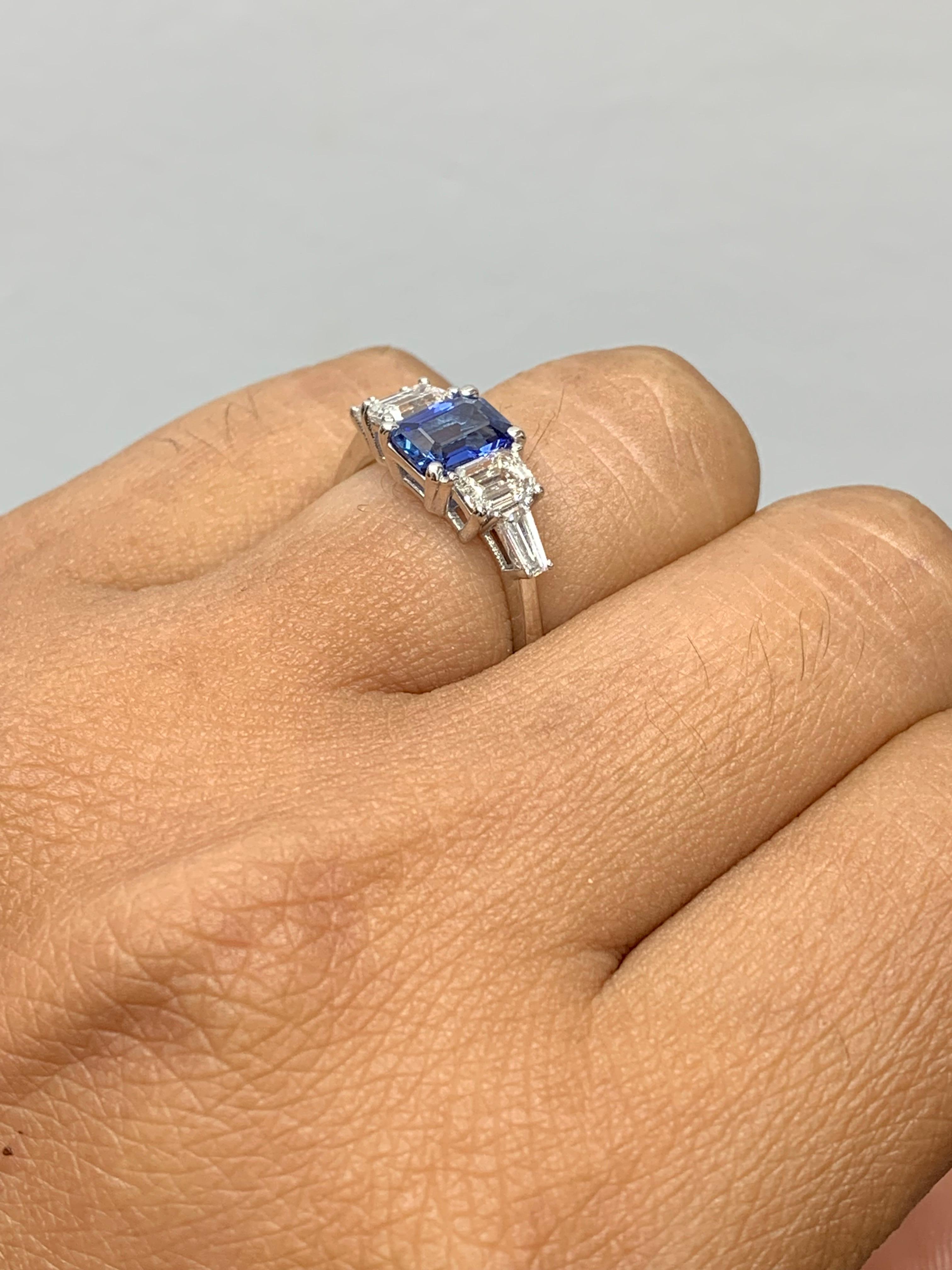 A stunning ring showcasing a rich intense emerald cut royal blue sapphire weighing 1.12 carats. Flanking the center stone are two emerald-cut diamonds weighing 0.64 carats and two baguette diamonds on each side weighing 0.21 carats in total, Made in