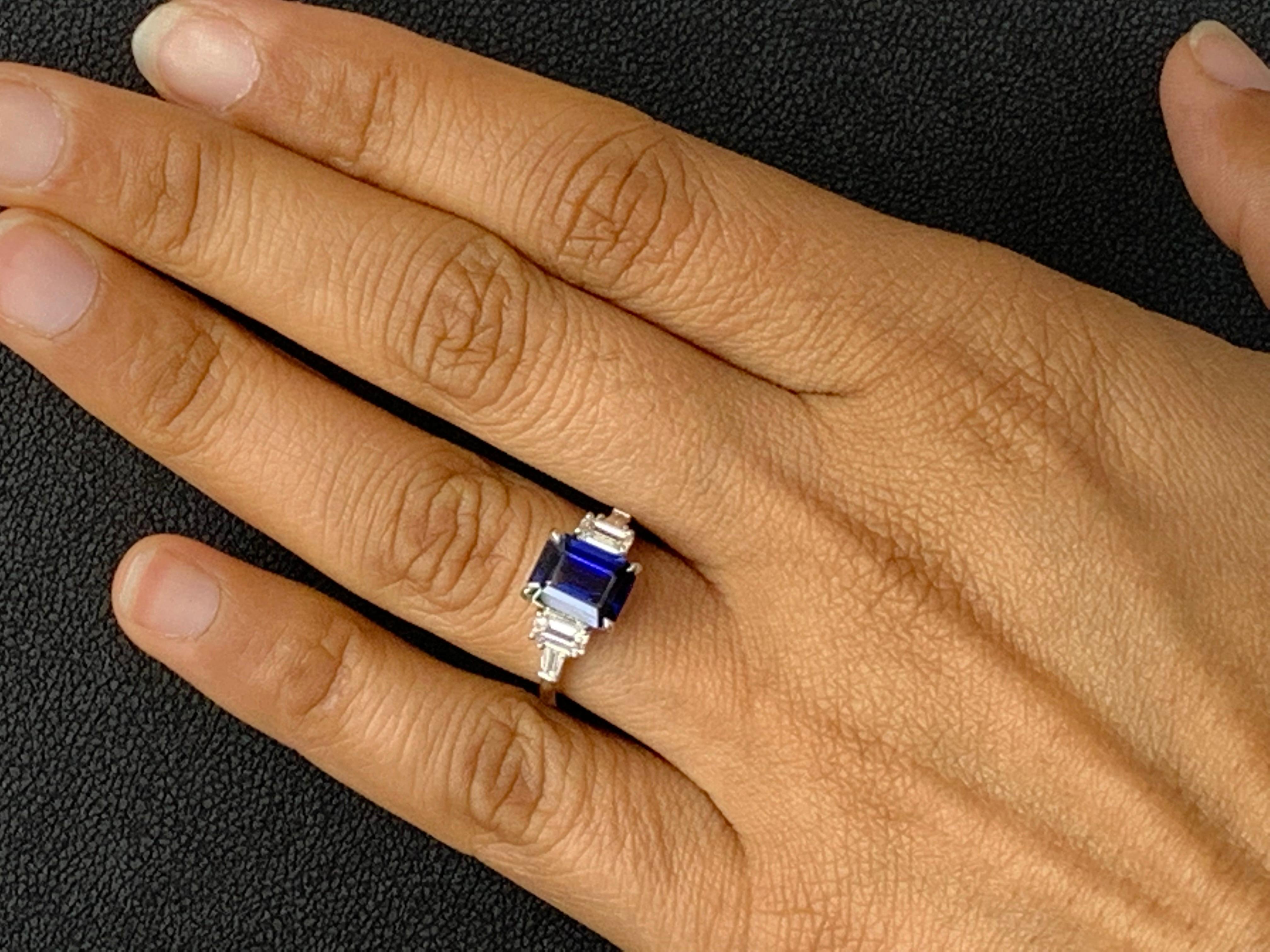A stunning ring showcasing a rich intense emerald cut blue sapphire weighing 1.12 carats.  Flanking the center stone are two emerald-cut diamonds weighing 0.64 carats and two baguette diamonds on each side weighing 0.21 carats in total, Made in 14K