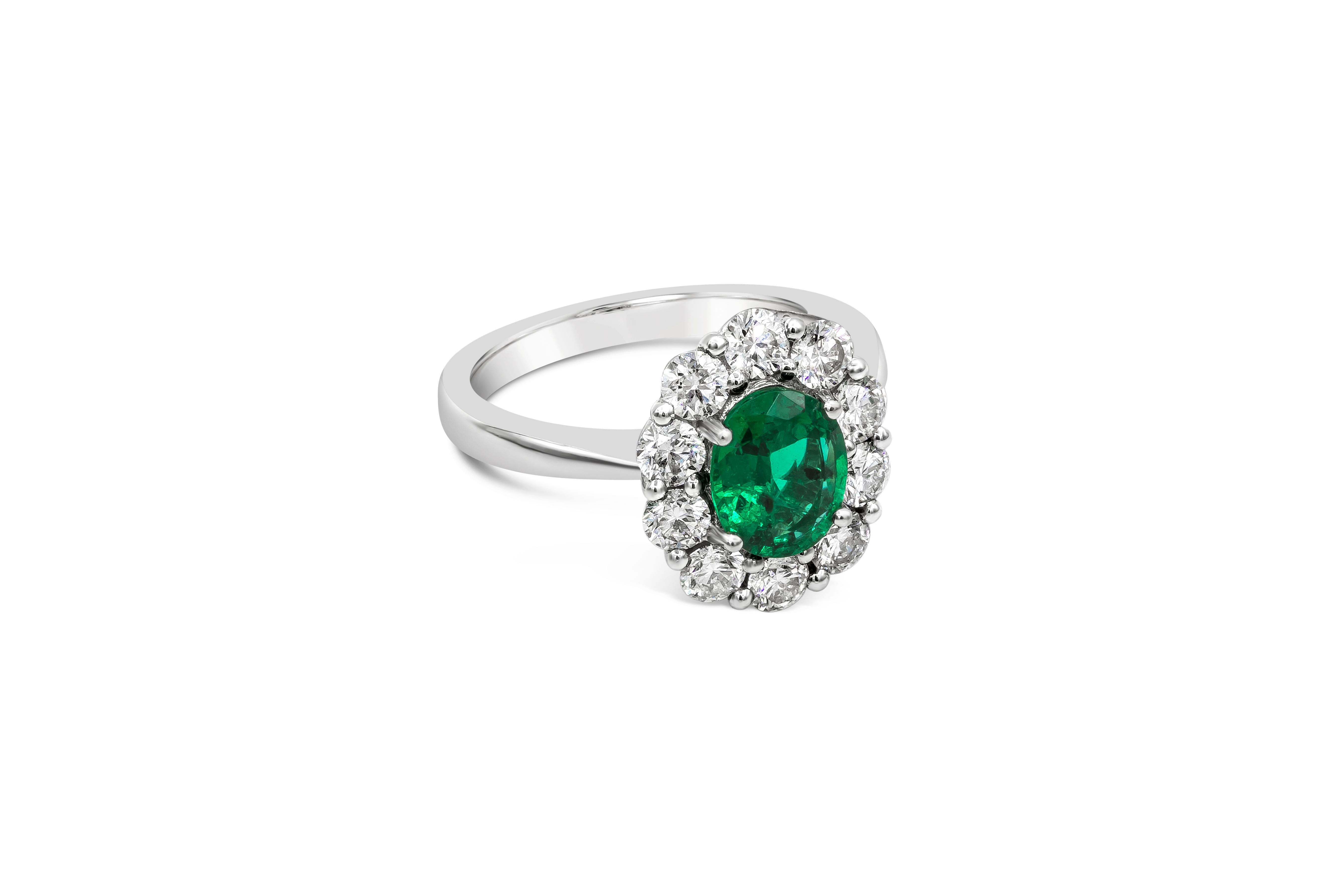 A beautiful engagement ring showcasing a 1.12 carat oval cut color-rich green emerald, surrounded by a single row of brilliant round diamonds weighing 1.09 carat total, set in an elegant floral-motif design. Made with 18K White Gold, Size 6 US