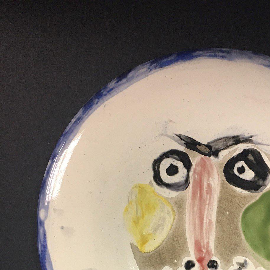 This piece is an A.R. round plate by Pablo Picasso, created in 1963.  Made with earthenware clay plate, decoration in engobe, and enamel under partial brushed glaze grey patina, yellow, green, black and blue. From the numbered edition of 150, shown