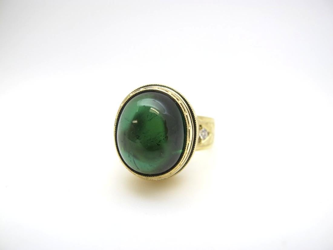 This stunning ring features a beautiful 11.28 carat tourmaline cabochon of saturated, pine-green color. The tourmaline is translucent with excellent clarity. Two brilliant cut diamonds add sparkle to the intricately engraved band. Handmade  in 18k