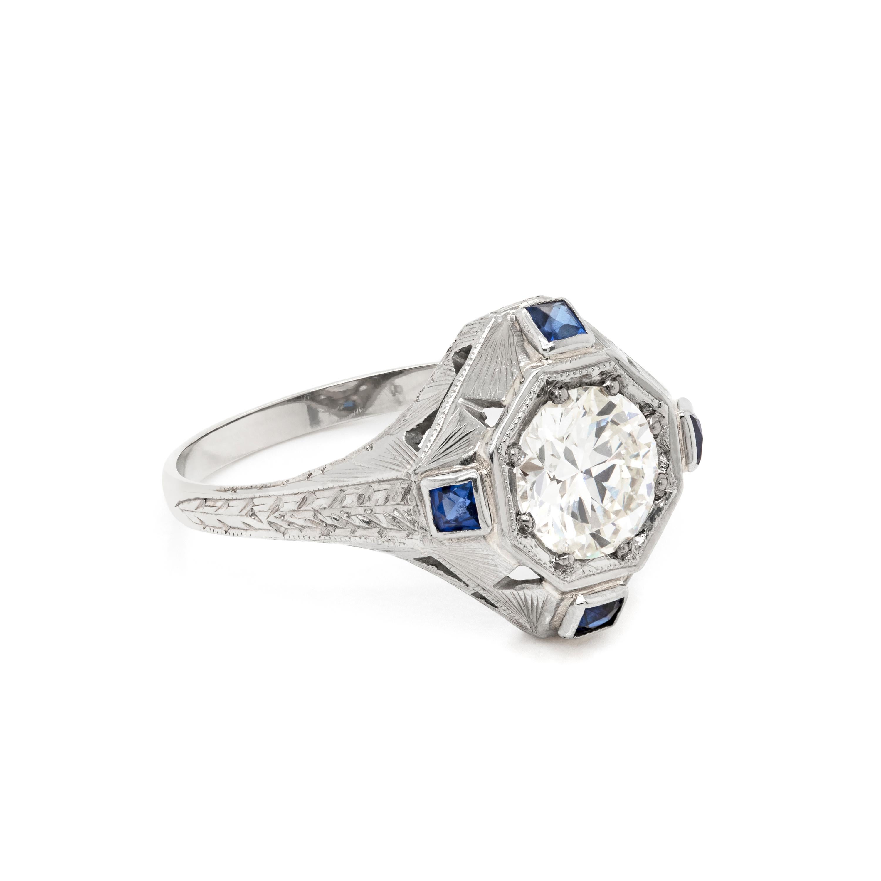 This 1930's Art Deco handmade target engagement ring features a 1.14ct transitional cut diamond, grain set into a square shaped target mount. The diamond is beautifully accompanied by four square shaped synthetic blue sapphires, rub-over set on each