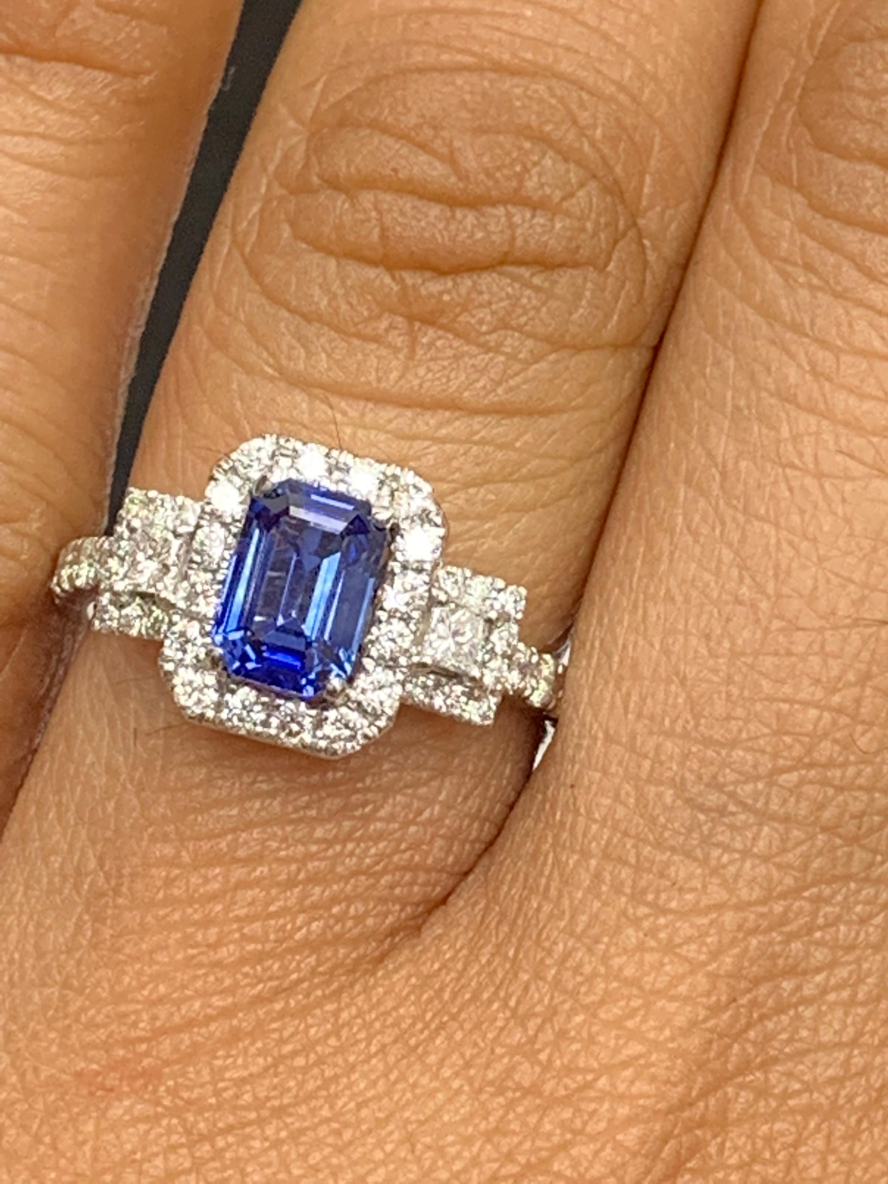 A stunning ring showcasing a rich blue emerald cut sapphire weighing 1.14 carats surrounded by diamonds. The center stone is surrounded by a row of 42 diamonds, weighing 0.58 carats total, with 2 princesses cut diamonds on each side weighing 0.12