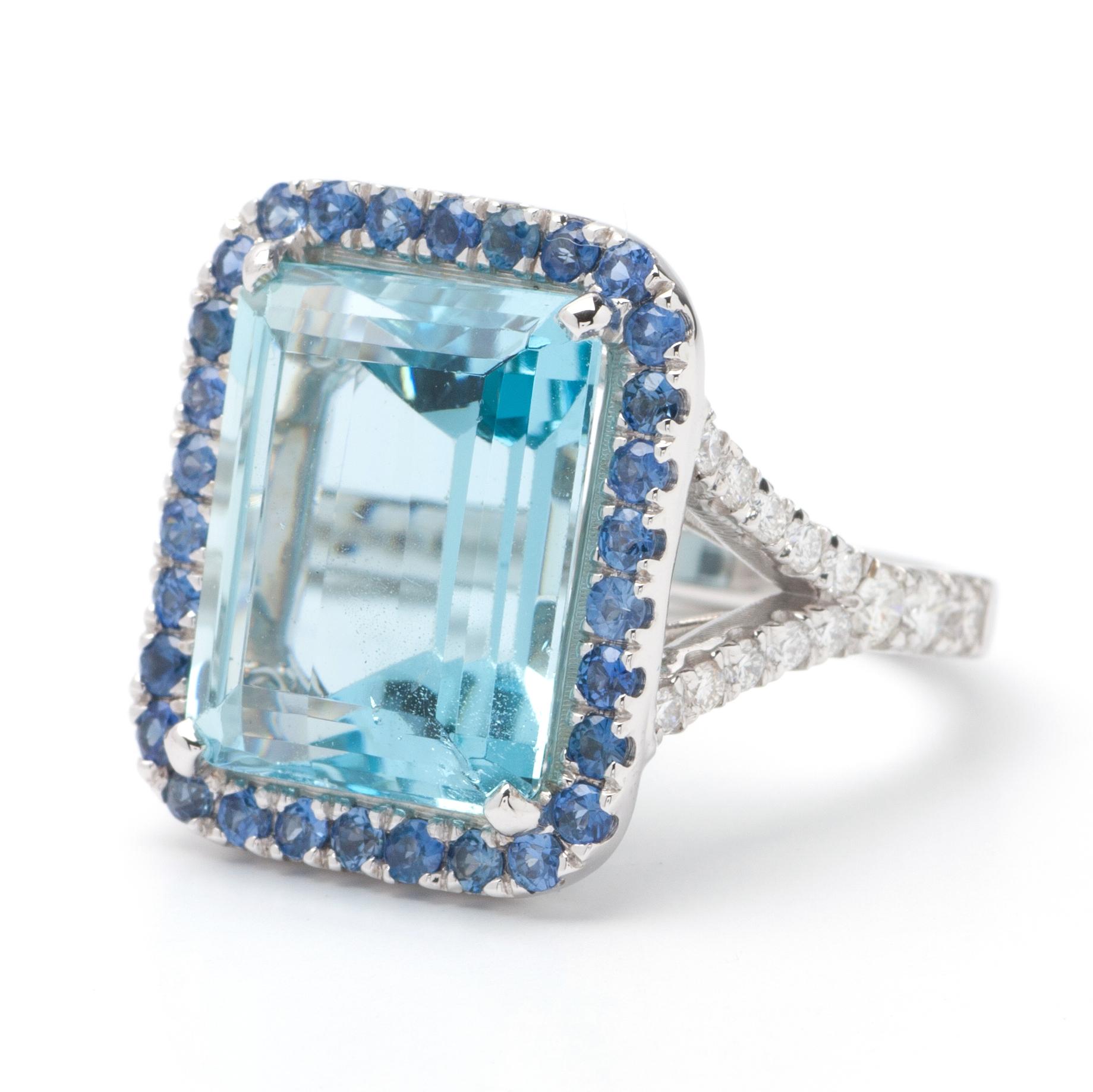 This ring features a halo design with .60ct of sapphires, a split shank of G color, VS1 clarity, and 1.03ct Round side diamonds set in 14K white gold. The center gemstone is an 11.40ct emerald-cut aquamarine stone, measuring 14.95 x 12.02 x 8.63mm.