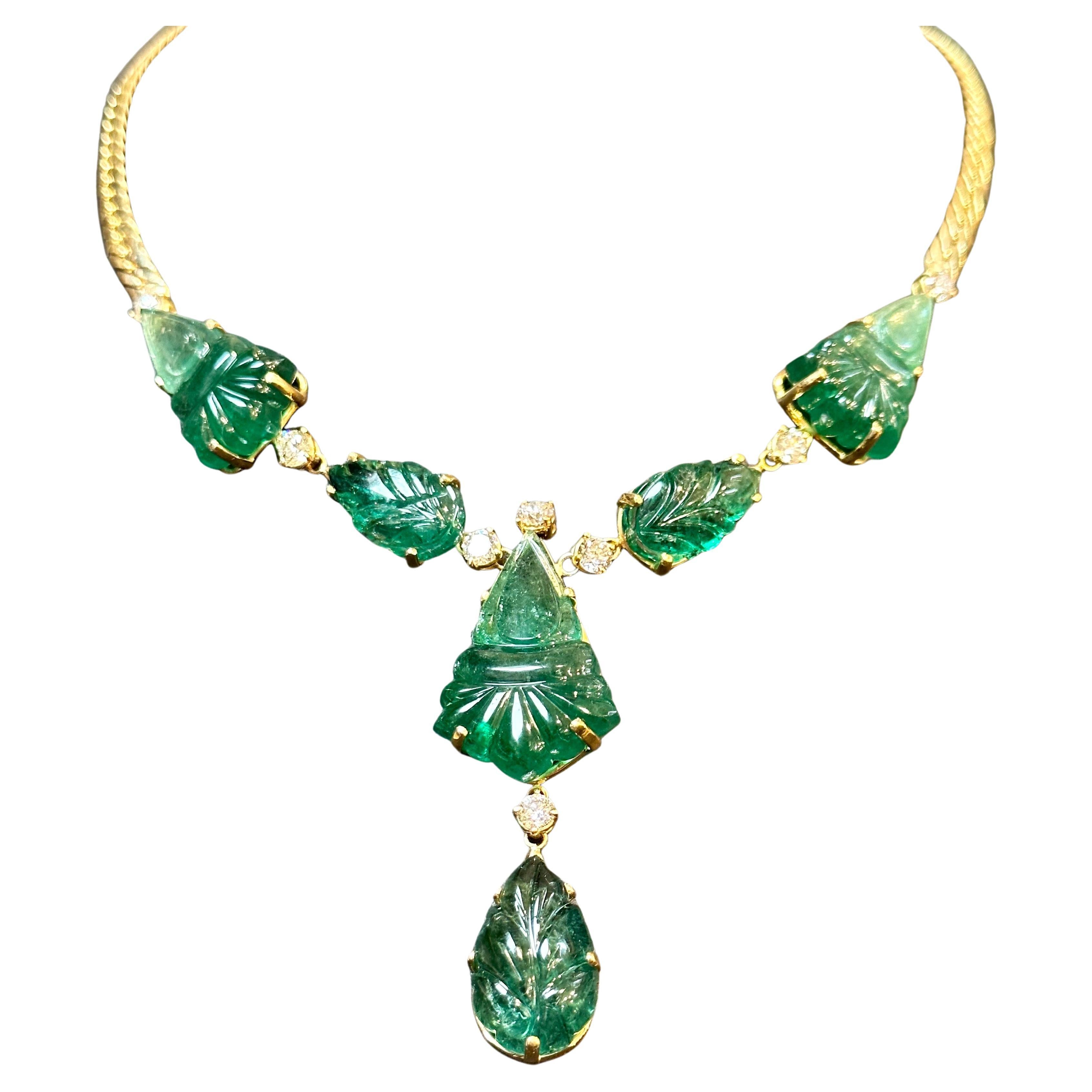 This stunning necklace features a remarkable combination of natural carved drop emeralds weighing 115 carats and 4 carats of solitaire diamonds. Crafted in 18 karat gold, the necklace showcases three intricately carved leaves and three larger pieces