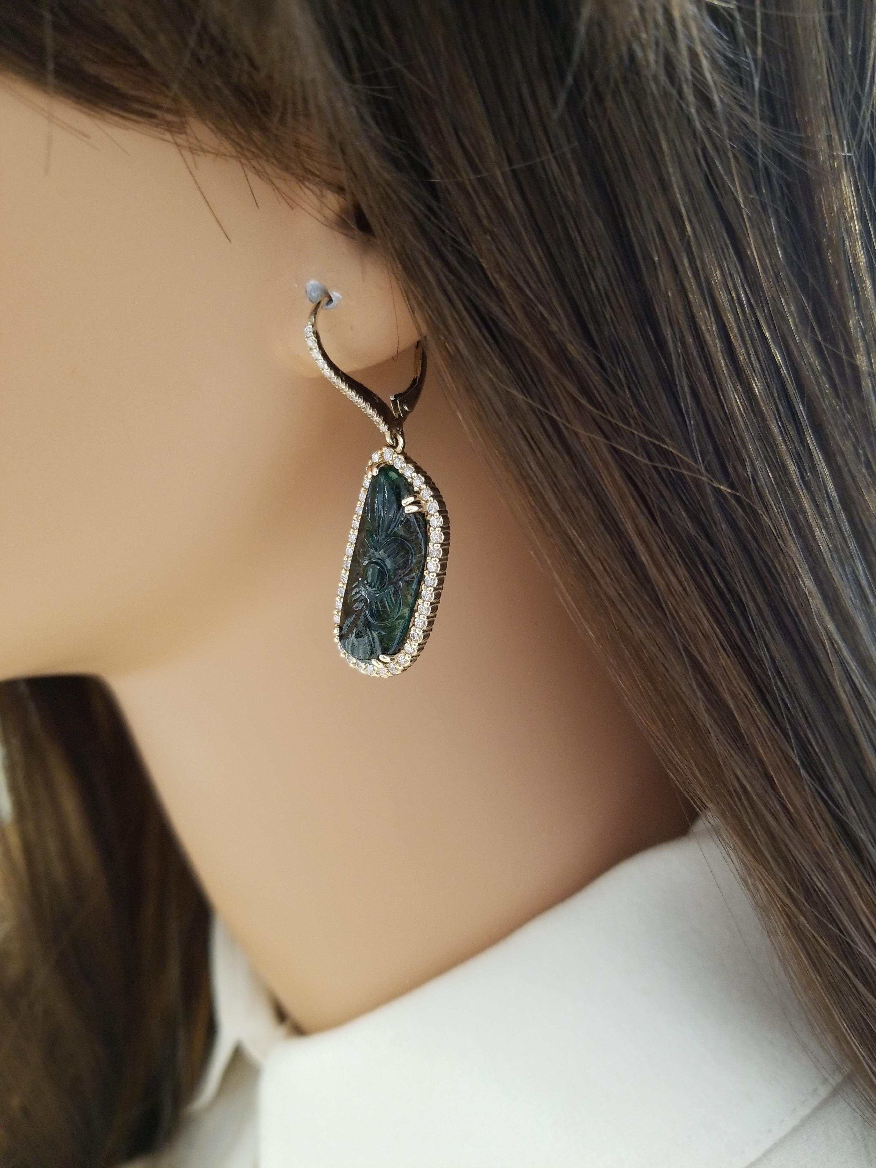 These artistically inspired drop earrings feature two hand-carved emeralds in double prong settings in the center totaling 11.58 carats. These lush forest-green, with speckles of blue, emeralds are framed by 100 sparkling round brilliant cut