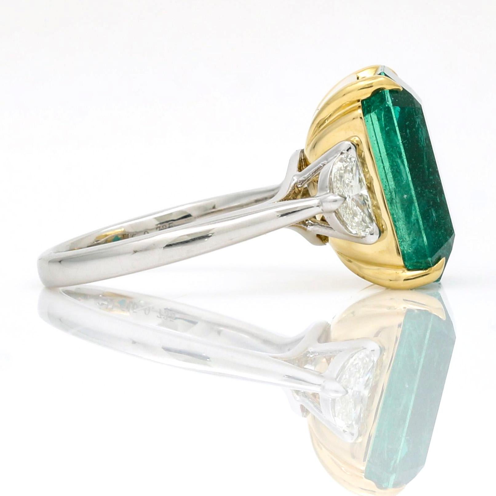 Women's emerald and diamond ring with a crescent-cut diamond on the sides crafted in 18k yellow gold and platinum. A large translucent emerald-cut emerald set in a yellow gold basket with a half-moon diamond on each side and a polished shank in
