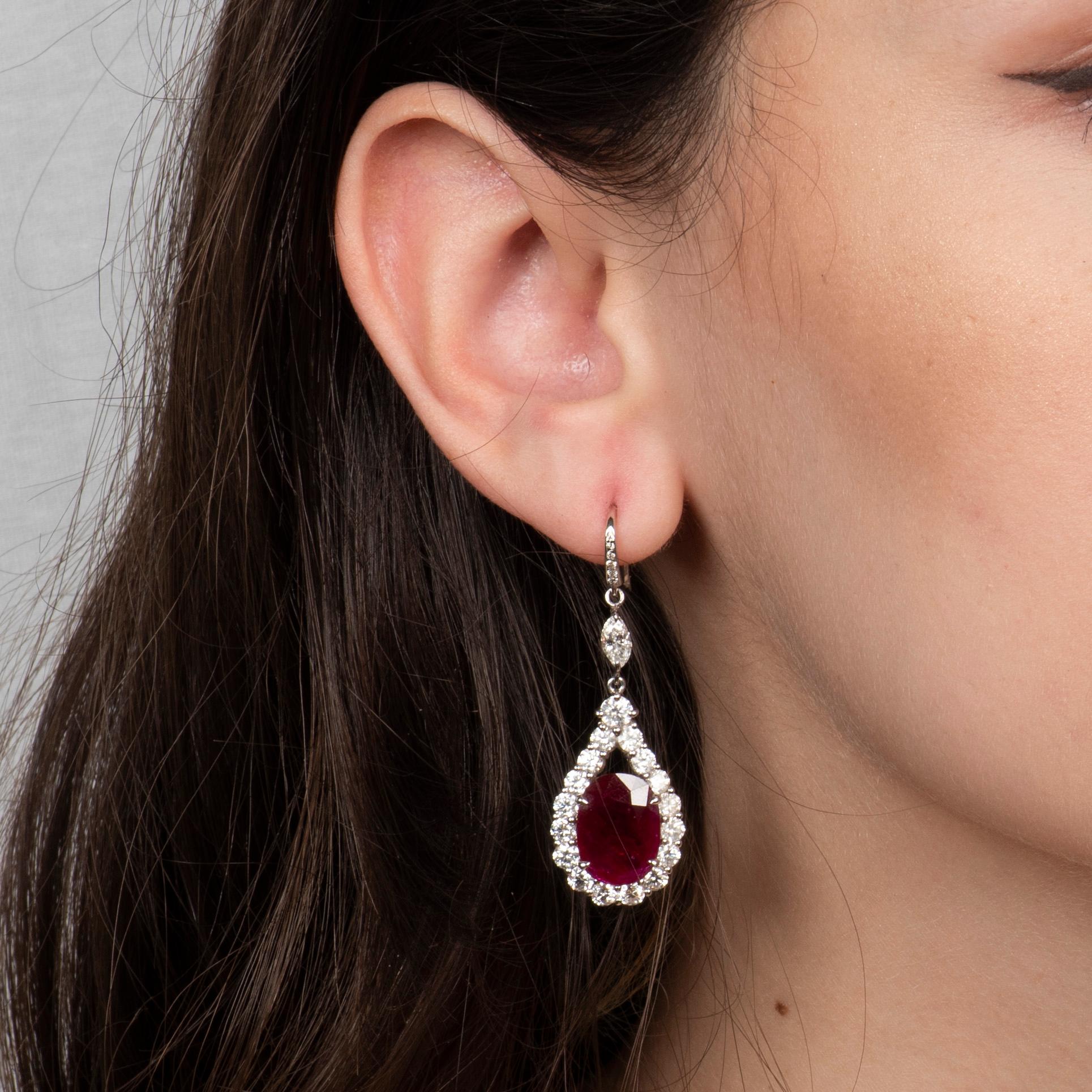 These gorgeous 11.85ctw natural oval cut rubies are surrounded by 4.49ctw in fine white round diamonds forming the halo in a pear form. These dangle earrings have great fluidity and swing freely, catching the light. They are set in 18kt white gold.