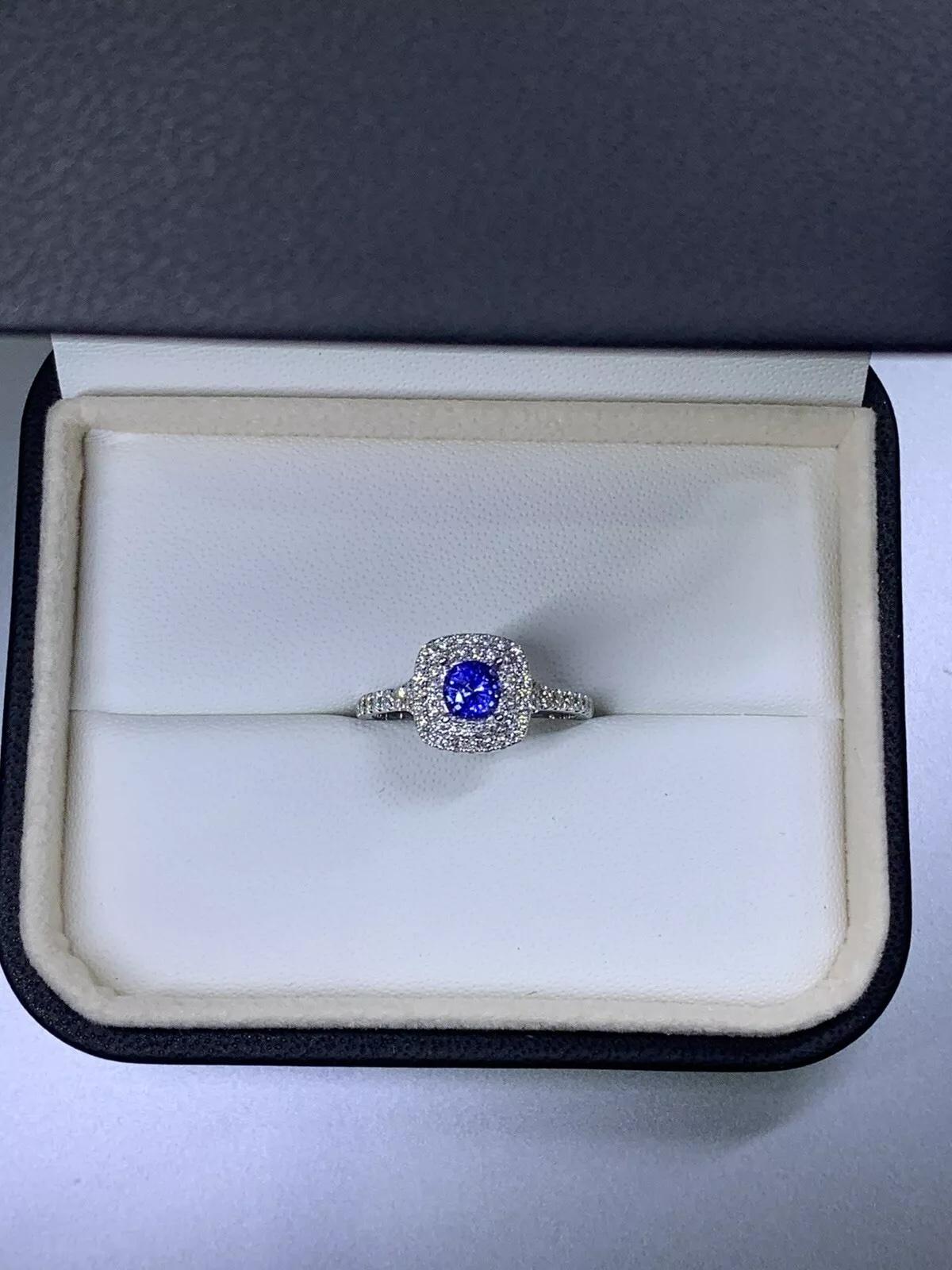 Cette magnifique bague de fiançailles saphir-diamant est un véritable chef-d'œuvre de solitaire. Réalisée en or blanc 18 carats, cette bague est ornée d'un superbe saphir de 1,15 carats de forme ronde, entouré d'un halo de diamants plus petits. La