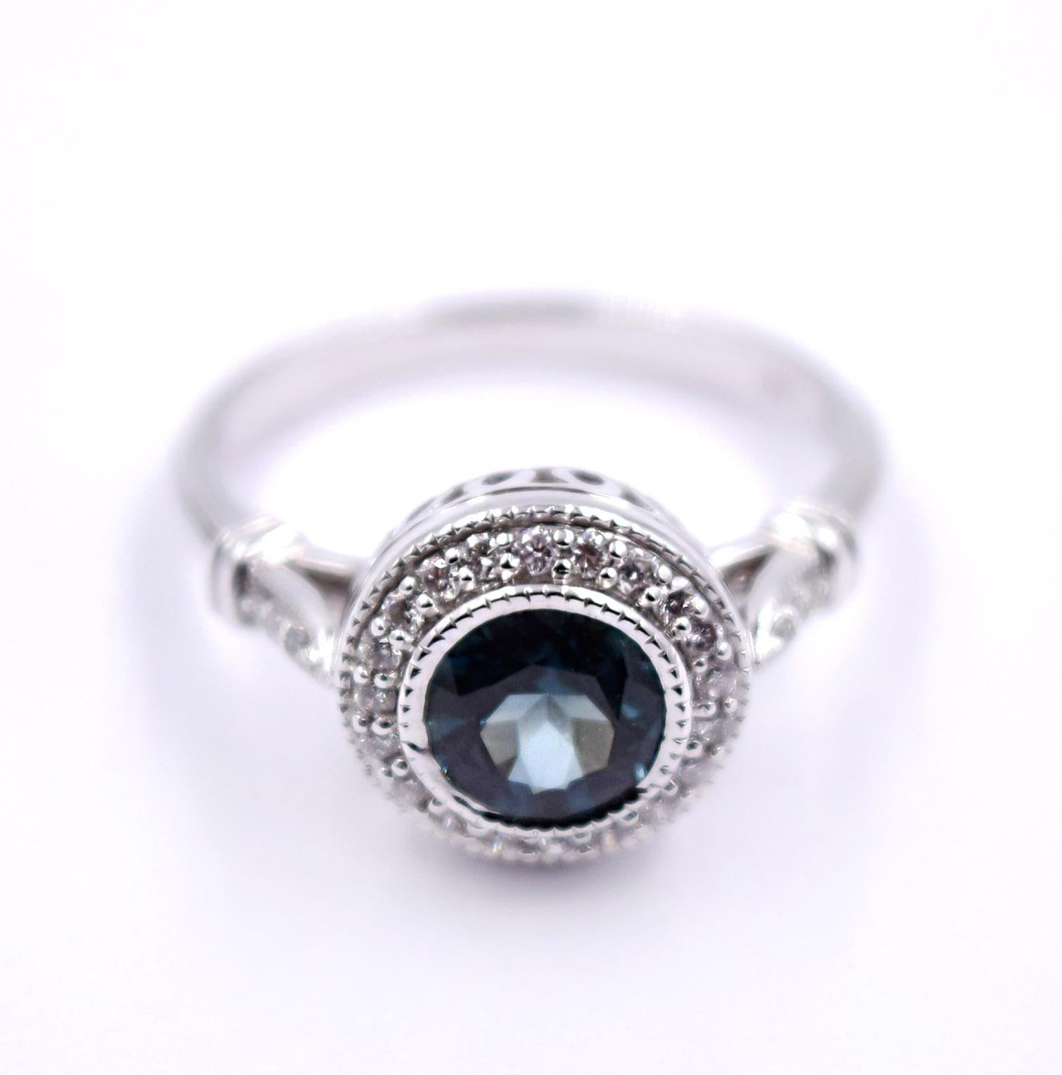 This beautiful vintage inspired ring features a 1.16 carat blue green sapphire center stone which is bezel set in 14 karat white gold. White diamonds surround the center stone in a beautiful halo setting, totaling 0.16 carats. The total weight of