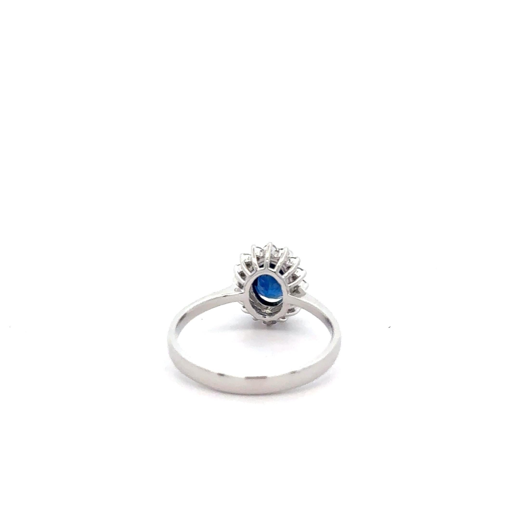 Ein klassischer und schlichter Ring mit einem blauen Saphir und Diamanten im Halo-Schliff. In der Mitte befindet sich ein natürlicher dunkelblauer Saphir von 1,16 Karat im Ovalschliff, der von 16 weißen, augenreinen Diamanten umgeben ist, die einen