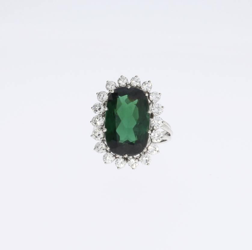 Europe, 1960's. Oval shaped deep green tourmalin weighing ca. 11,6 carat surrounded by 18 brilliant-cut diamonds with a total weight of ca. 1,18 carat, clarity VS-VVS1. Mounted in 18 K white gold. Total weight: 7,55 grams. 
Measurements: 0.91 x 0.71