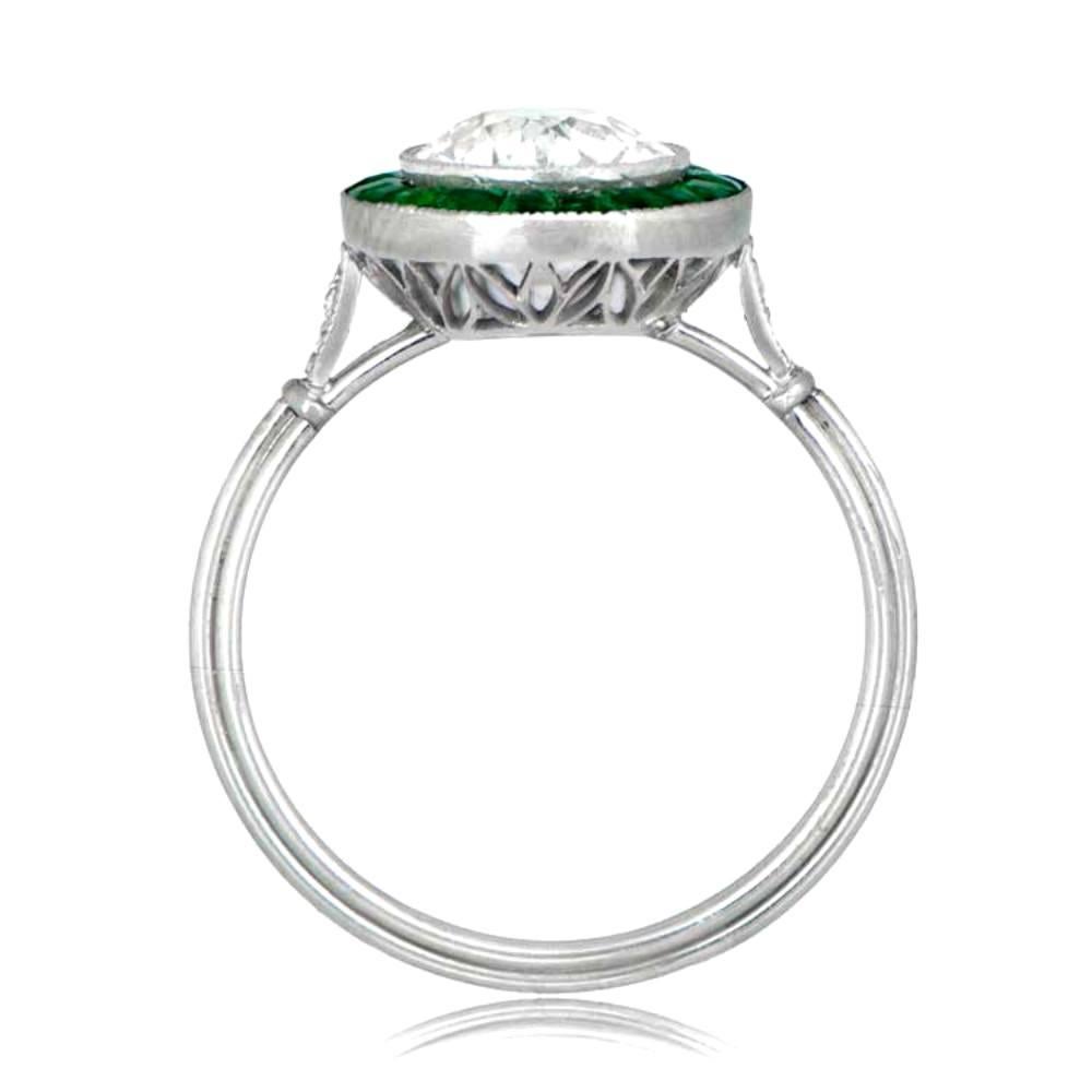 This elegant ring boasts a 1.16-carat old European cut diamond surrounded by a halo of beautifully arranged calibre emeralds and delicate milgrain detailing. The lower gallery is adorned with fine arch-motif openwork filigree, and both shoulders are