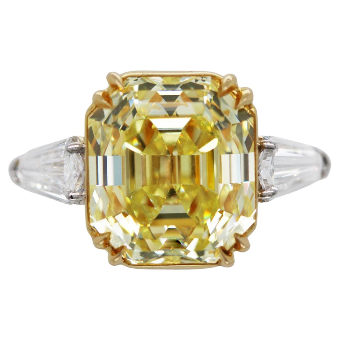 An elegant 11.71 carat Fancy Intense Yellow emerald-cut diamond engagement ring, with white bullet-cut side stones (TCW 1.15) set on 18k yellow gold and platinum. The rectangular emerald cut center stone is an evenly colored fancy intense yellow