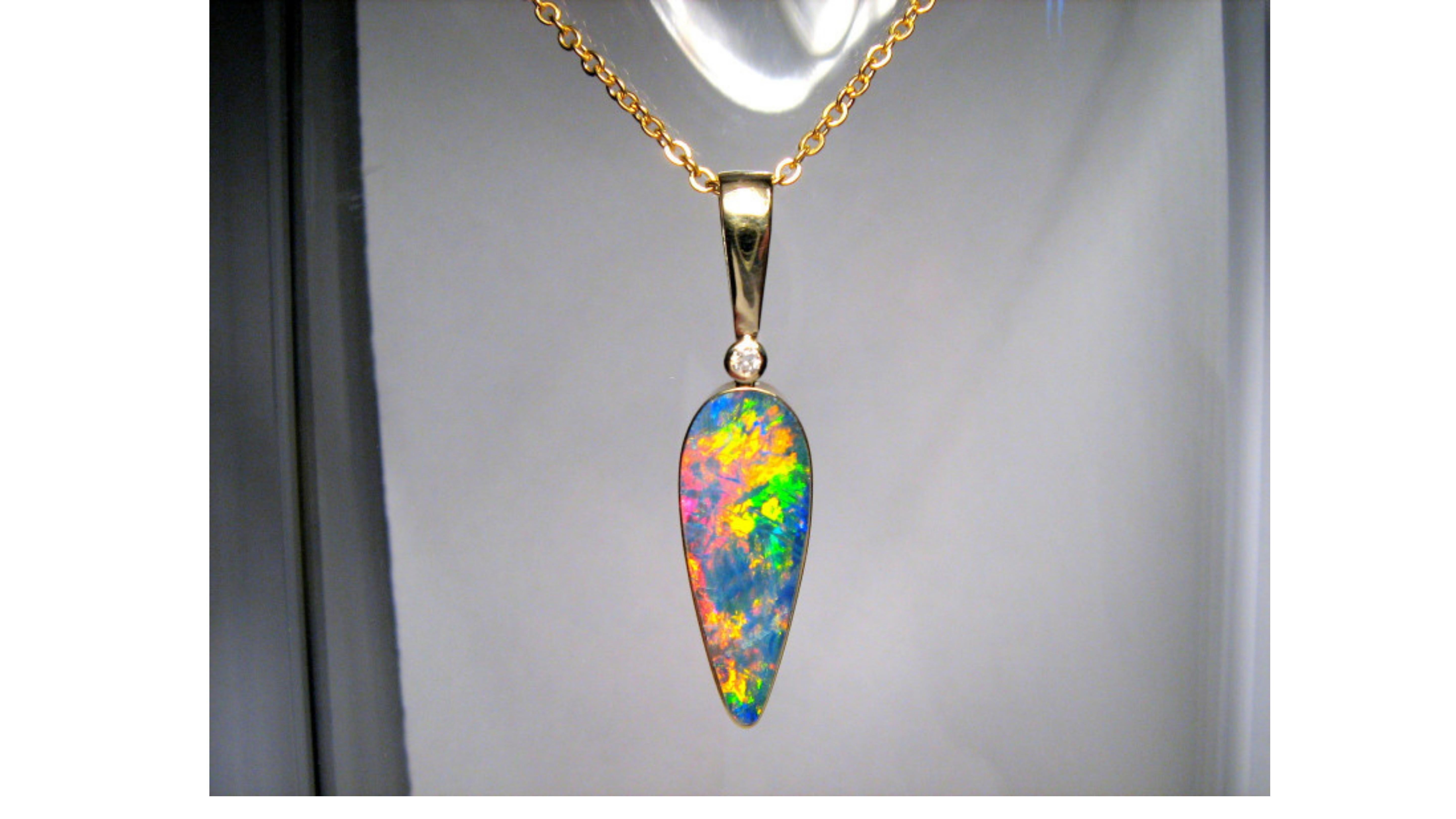 

Australian Opal Necklace 14 Karat Yellow Gold . This shows off very bright colors  Blue Yellow Green Orange Pink Red and really does stand out with the diamond too at the top. It comes from Coober Pedy in South West Australia.   A true one of a