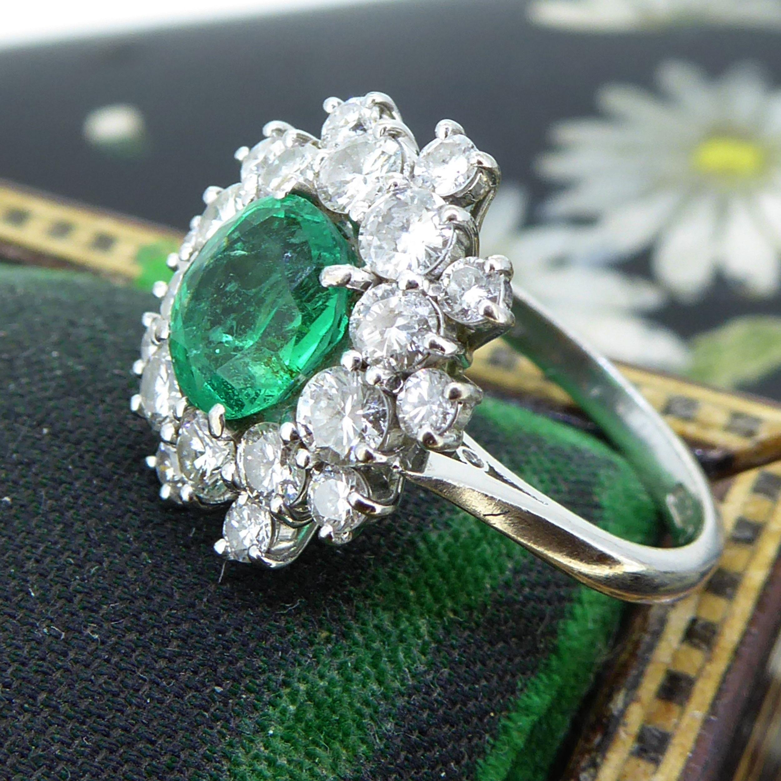 An emerald and diamond vintage ring that centres on an oval shaped, mixed cut medium green emerald estimated to weight 1.18ct and measuring 7.55mm x 6.50mm x 4.10mm deep.  The emerald sits in a white claw setting to a surround of 20 brilliant cut