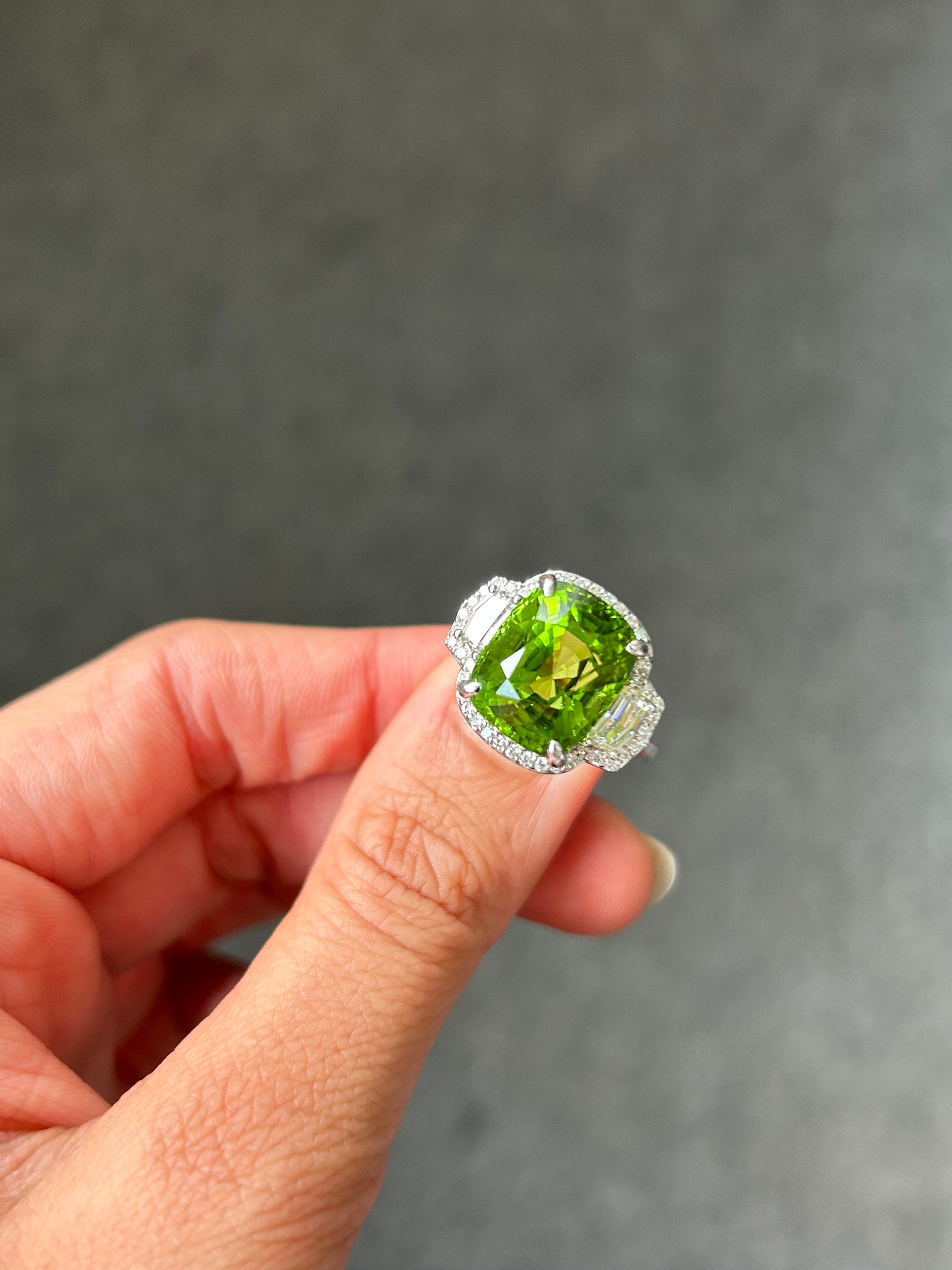 Top quality 11.96 carat Burmese Peridot with 0.61 carat Cadillac shaped side stone White Diamonds, and 0.34 carat Diamond halo. The center stone is an ideal green color, absolutely transparent with no inclusions and amazing luster/shine. The ring is