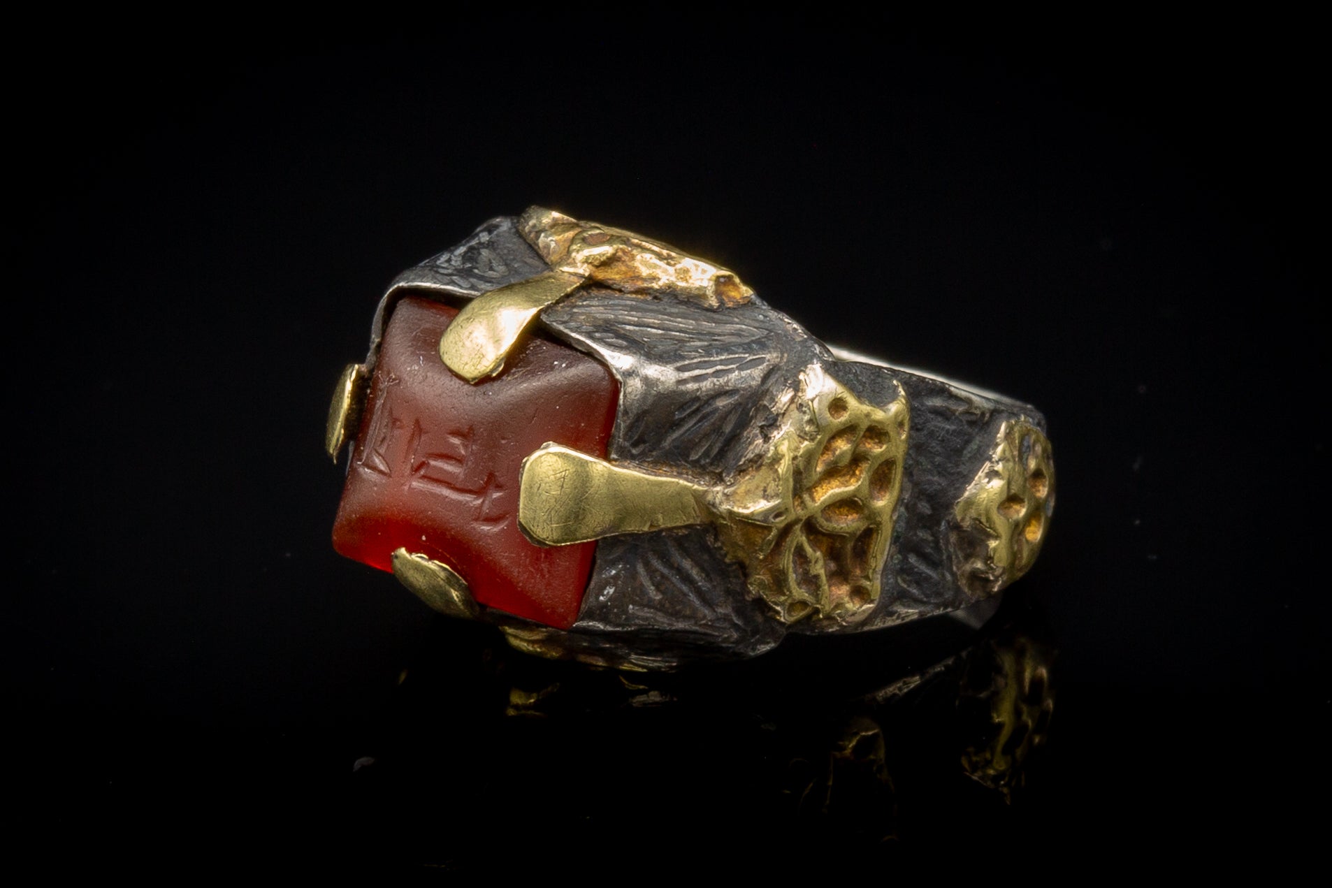This incredible piece dates to the 11th century Seljuk dynasty. The carnelian intaglio is set within a typical Seljuk tapered rectagonal bezel with a four-pronged gold setting soldered to the outside of the bezel. Applied and pierced high carat gold