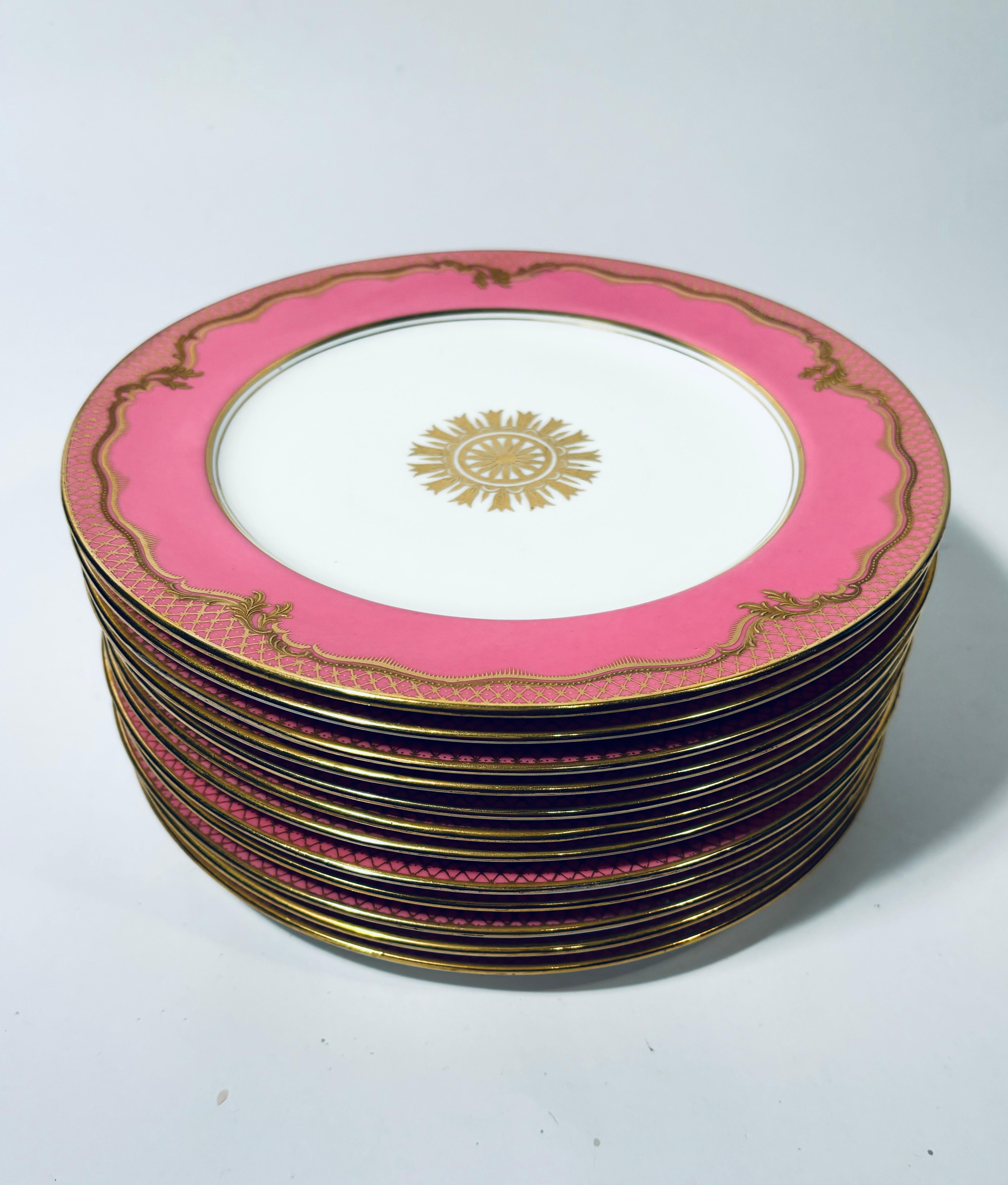 A set of vibrant pink and raised gold plates in wonderful antique condition. This set features raised gilt enhanced designs on their collars and a center gold medallion. Produced at the turn of the last century by Aynsley, England. The perfect size