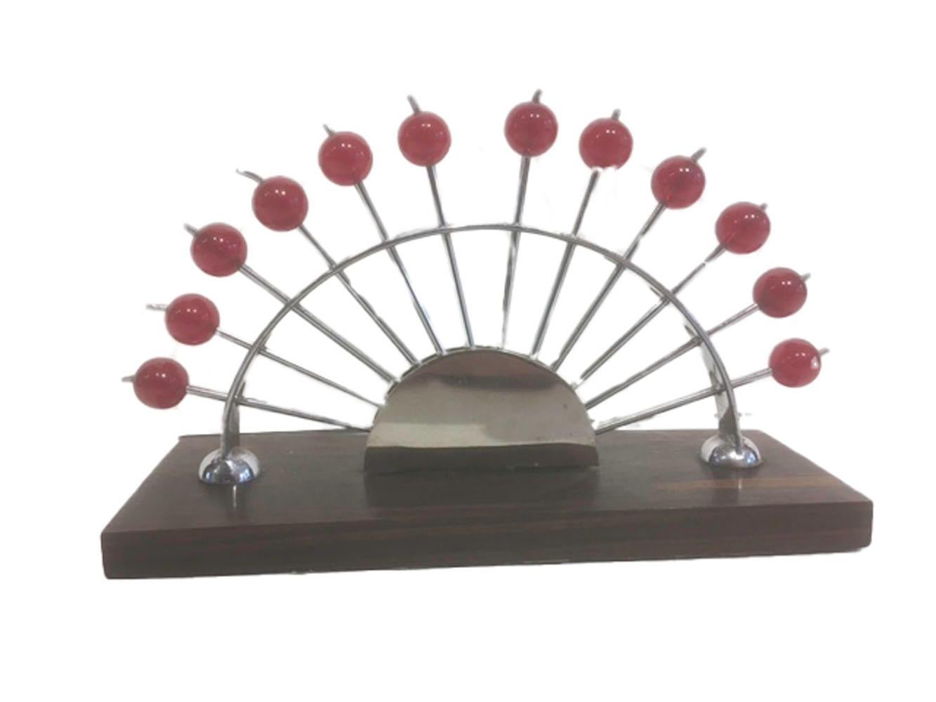 Art Deco cocktail picks in a fan-form stand. The forked chrome picks with red ball tops finished with a small chrome stem. The arched holder has 12 holes to accommodate the picks with the points enclosed in a semicircular chrome guard, all set on an