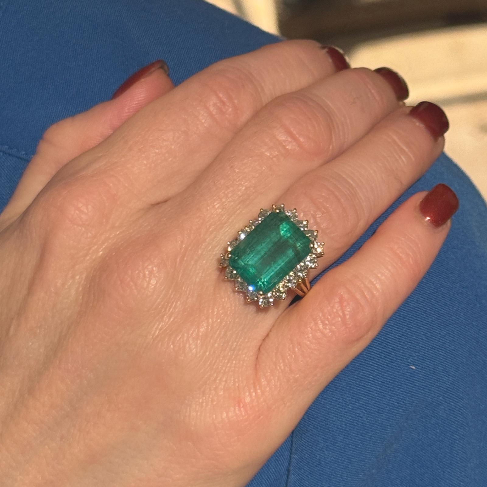 This breathtaking 18k yellow gold ring showcases a stunning 12-carat emerald-cut emerald as its centerpiece, celebrated for its vibrant green hue and timeless elegance. Surrounding the emerald are 18 round brilliant-cut diamonds, totaling