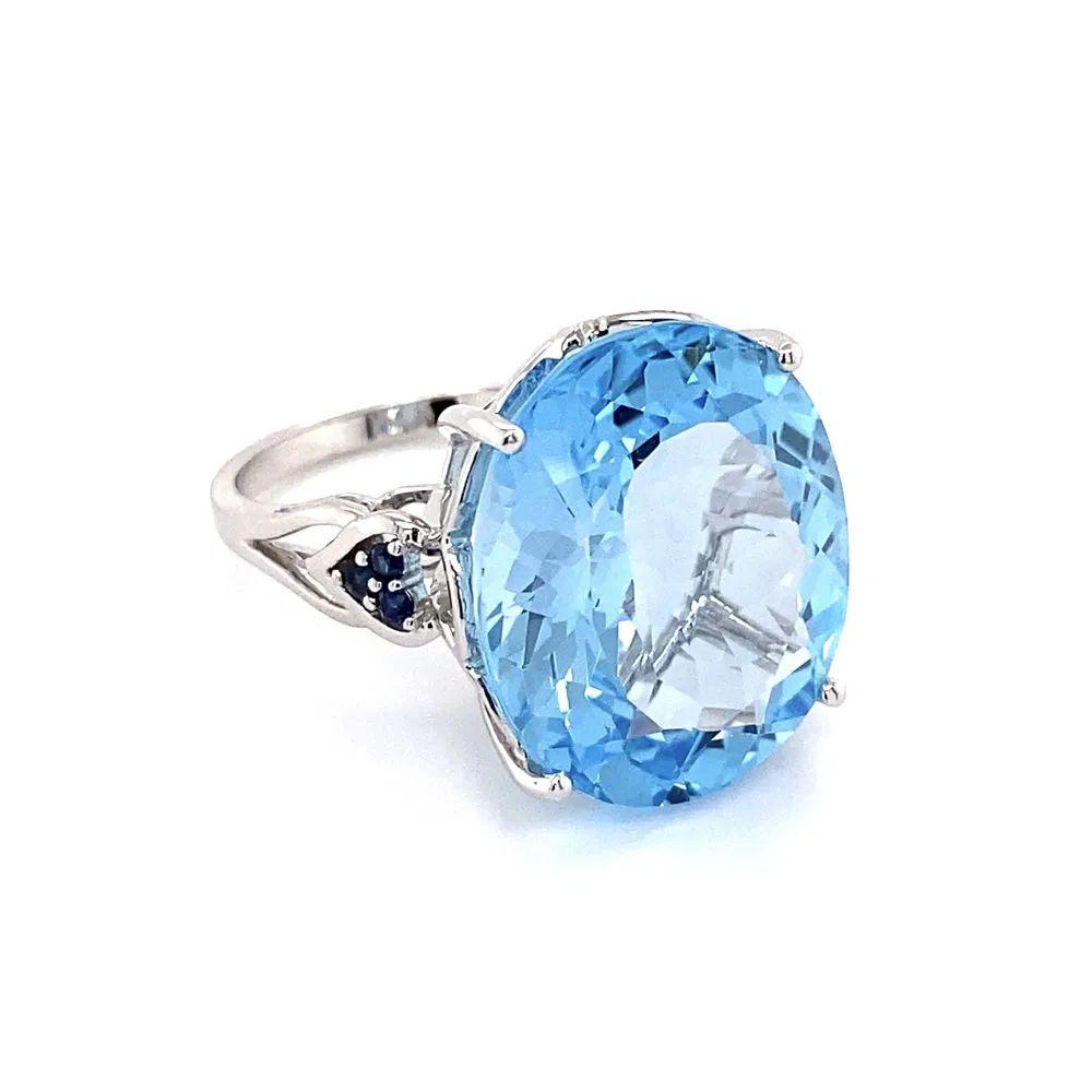 Simply Beautiful! Vintage Oscar Worthy Oval Blue Topaz and Sapphire Solitaire Gold Cocktail Ring. Centering a securely nestled Hand set Impressive 12 Carat Oval Blue Topaz. Accented with Sapphires, approx. .10tcw. Finely Hand-crafted 14K White Gold
