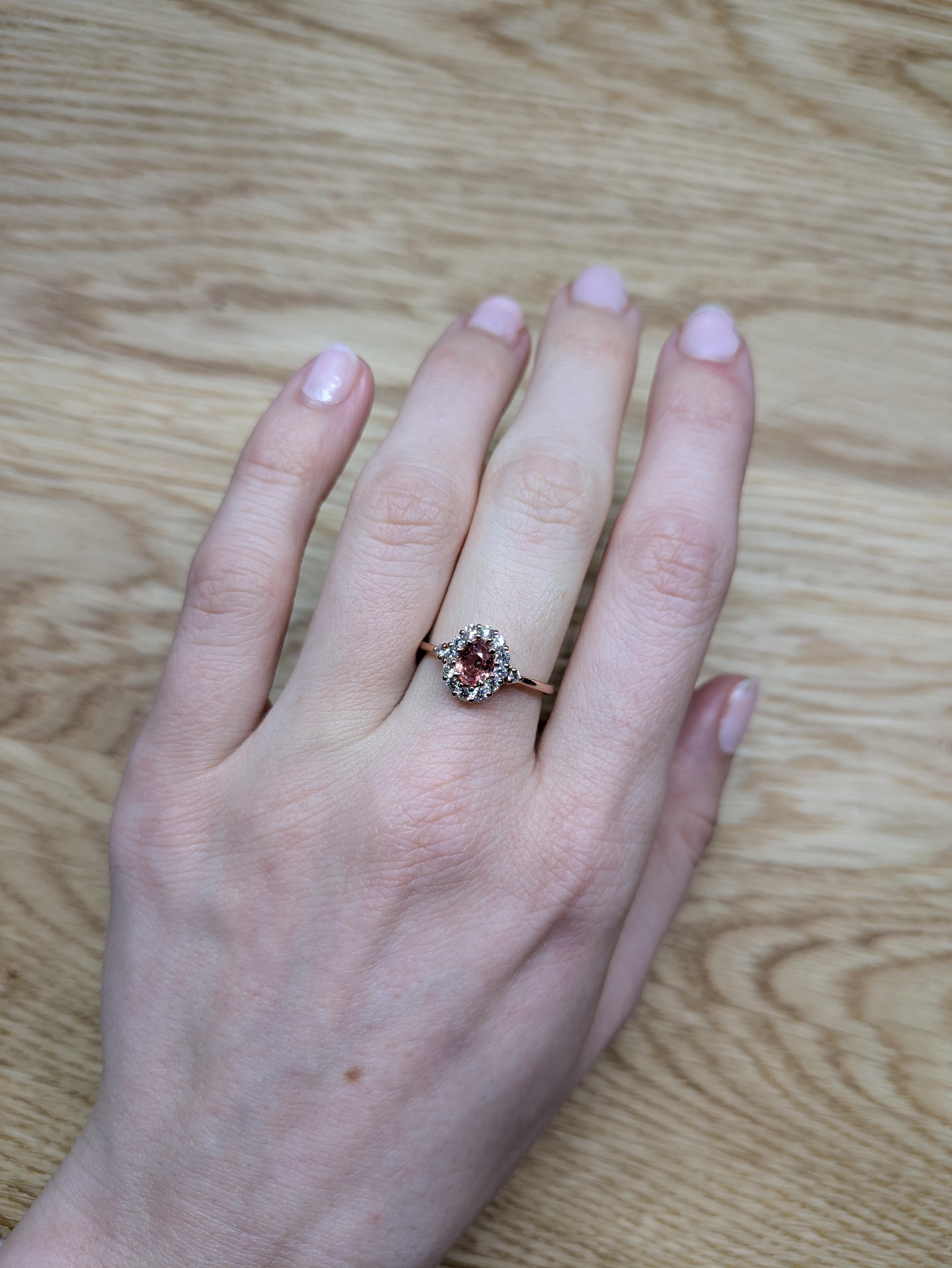 This exquisite Padparadscha sapphire ring features a rare, peachy-pink oval sapphire, encircled by a dazzling halo of earth-mined diamonds. Set in solid 14K rose gold, the warm hues enhance the gem’s natural radiance, creating a romantic and