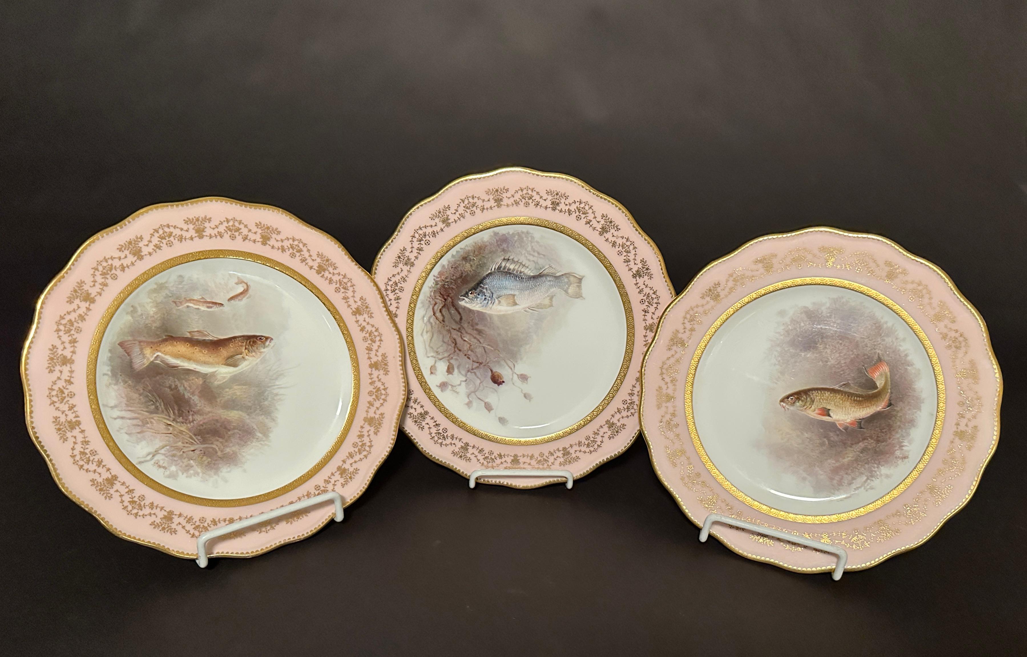 Juego de 12 platos de porcelana con peces pintados a mano por Cauldon, Inglaterra, para Higgins & Seiter, Nueva York.  Conjunto de doce platos de pescado elaboradamente pintados, cada uno con escenas de diferentes peces, artista firmado D. Birbeck.