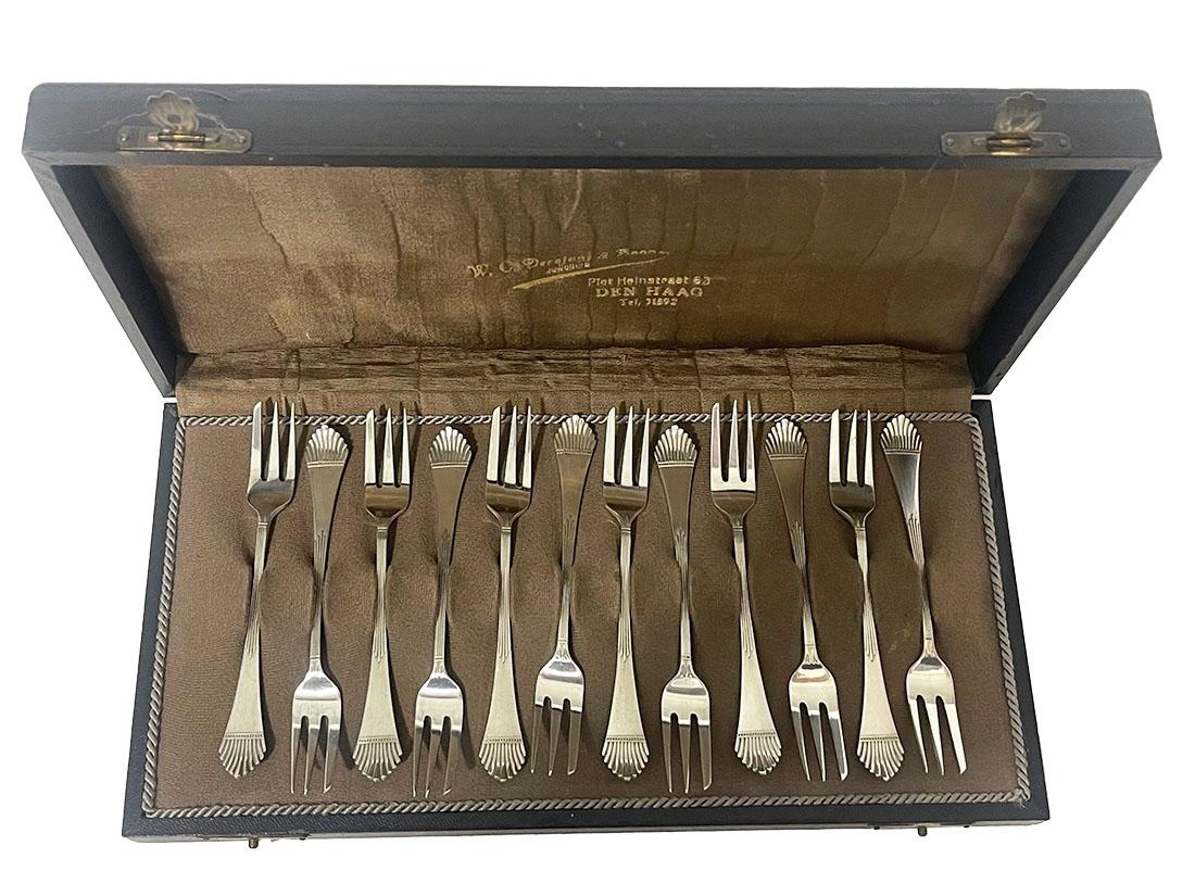 12 forchette da pasticceria in argento olandese di Gerritsen & Van Kempen

Queste 12 forchette da pasticceria olandesi in argento hanno delle linee in rilievo sul manico con una finitura a ventaglio. 
Queste forcelle sono il modello 14 (prodotto tra