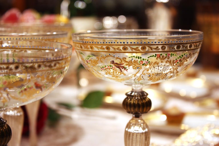 This is a rare set of 12 Venetian handblown champagne goblets made by Salviati. The coupe shape is large and dramatic and is decorated with the iconic Salviati pattern of multicolored enamel birds and gilded baskets of fruit surrounding the bowl.