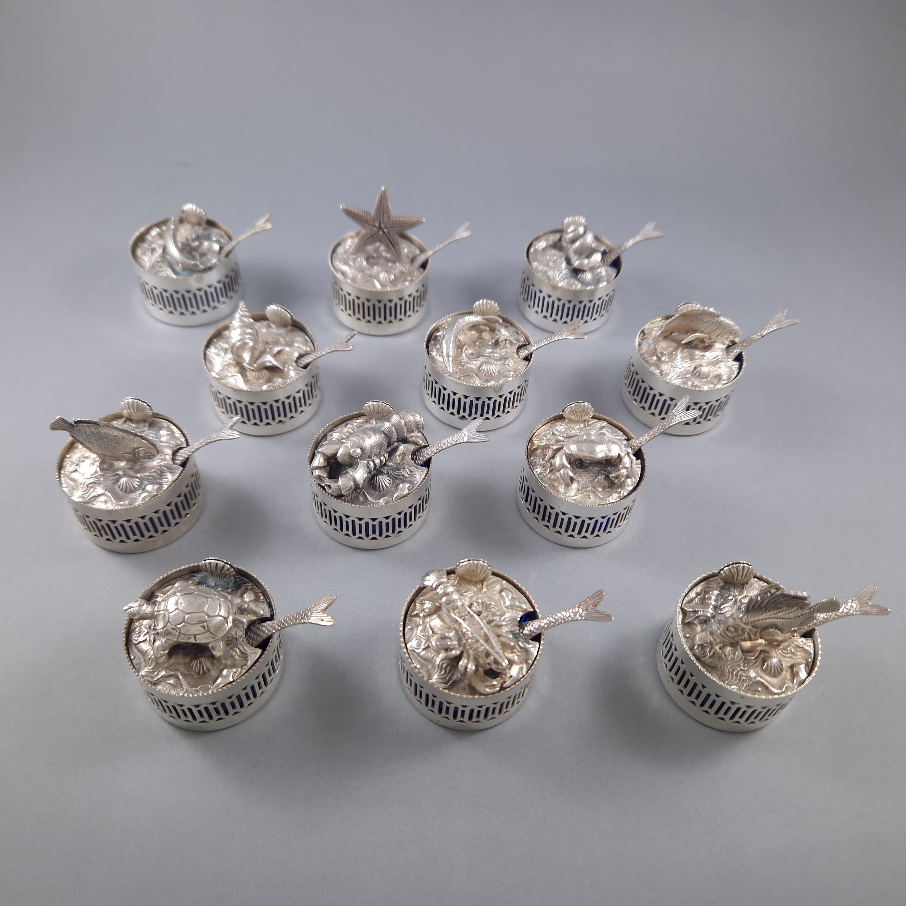 Beautiful set of 12 individual salt cellars / place card holders in sterling silver 
The interior in blue crystal, the lids finely decorated with marine animals, the shovels decorated with fish and shells Silver hallmark 800 
Diameter: 3.9 cm