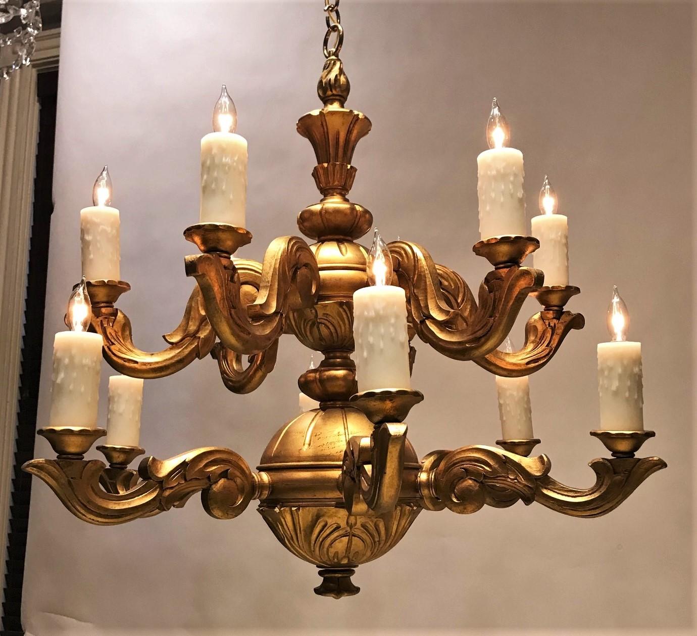 This striking chandelier is hand carved wood and hand gilded. The 12 lights have poly-beeswax candle covers. The fixture takes candelabra-base bulbs of up to 40 watts each. Hanging hardware, ceiling cap, and one foot of chain included