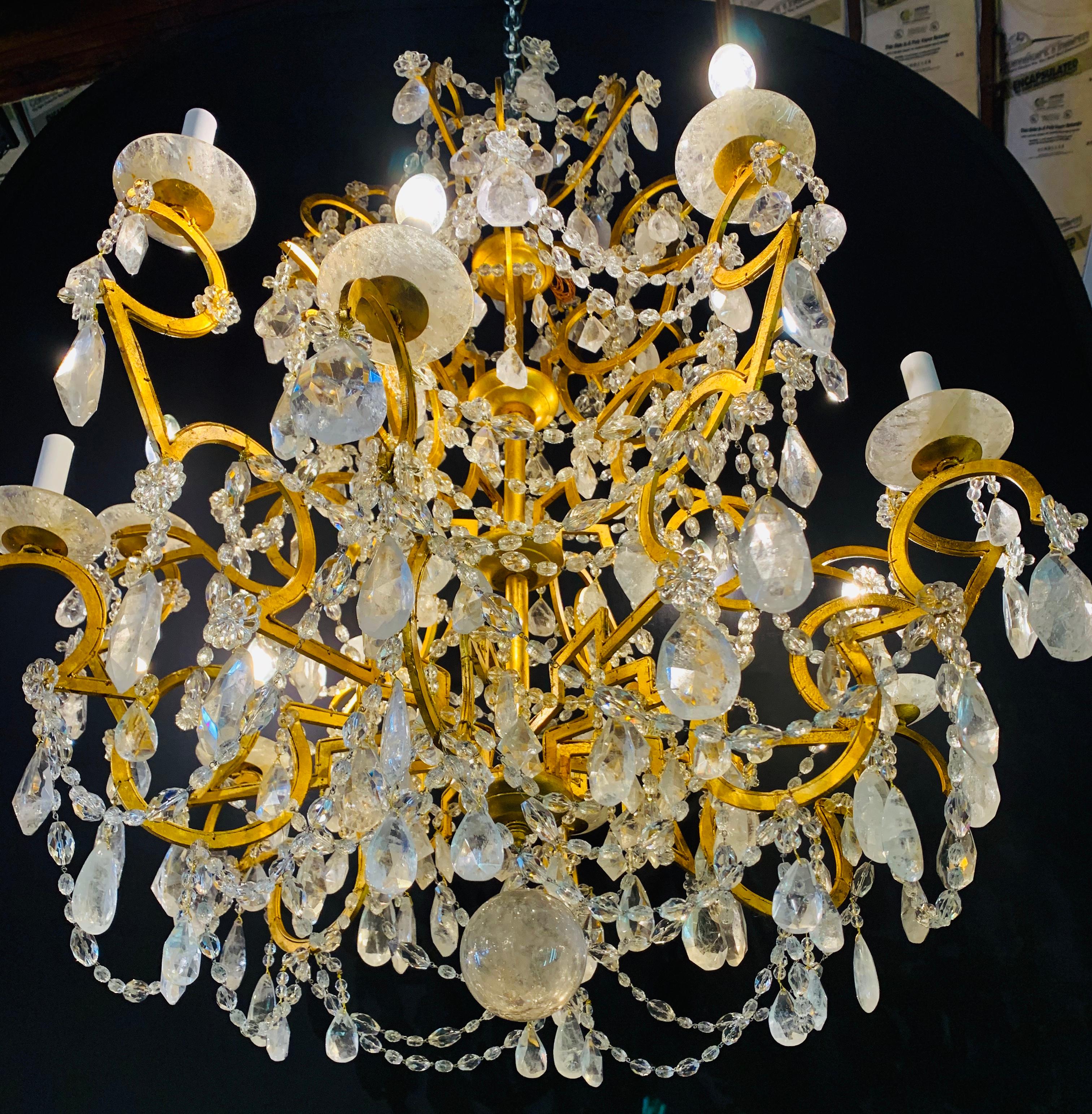 12 Light Gilt Metal Chandelier Having Multiple Rock Crystal Prisms in the Hollywood Regency Style. This large and impressive recently rewired chandelier has fine rock crystal prisms and rock crystal bobeches on all arms. The entire frame has been