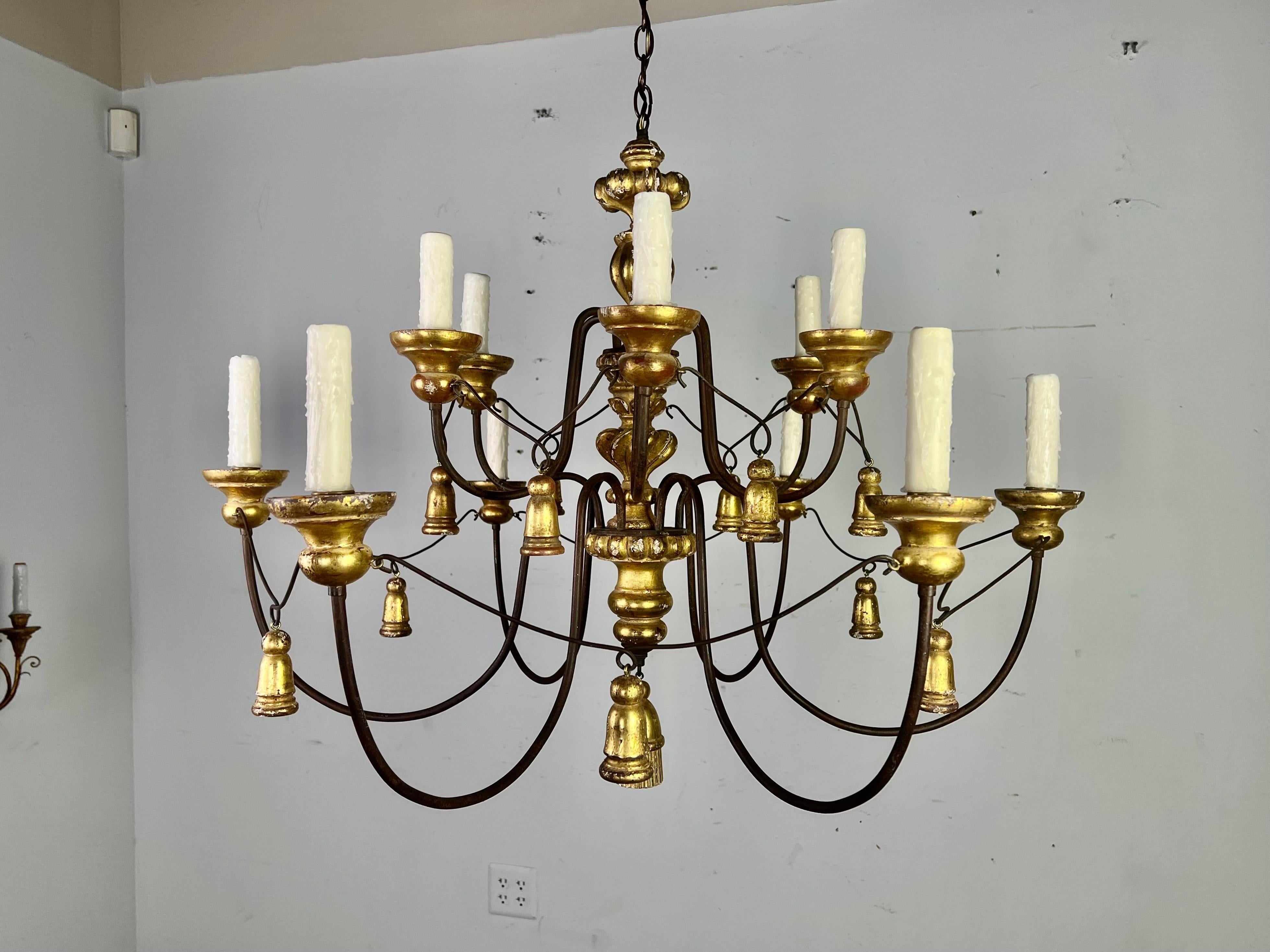 Stunning giltwood & iron 12 light Italian style chandelier with drip wax candle covers. There are garlands of wooden tassels dancing throughout the fixture. It is in good condition, rewired, and includes chain & canopy. Perfection.