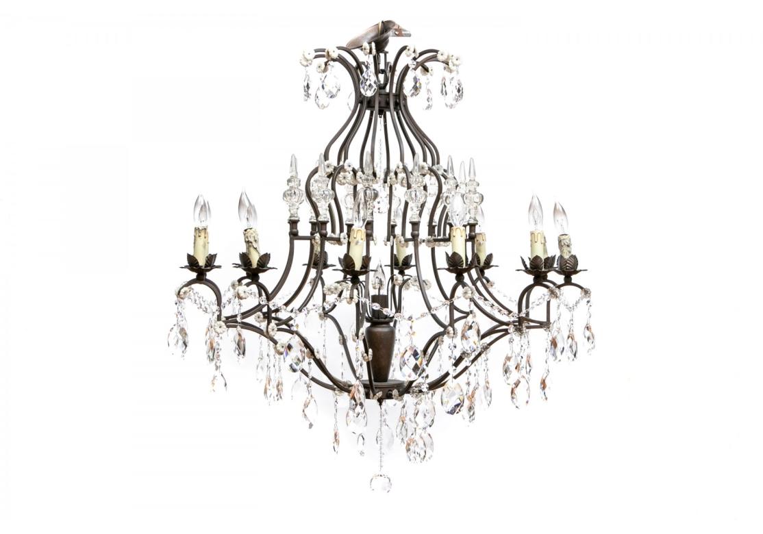 A shaped standard with pendant crystals and white rosettes on the top and tall pointed crystals in the middle. The lights with tole bobeches and faux candles, the crystal chains between them with pendant faceted crystals. The lower vasiform support