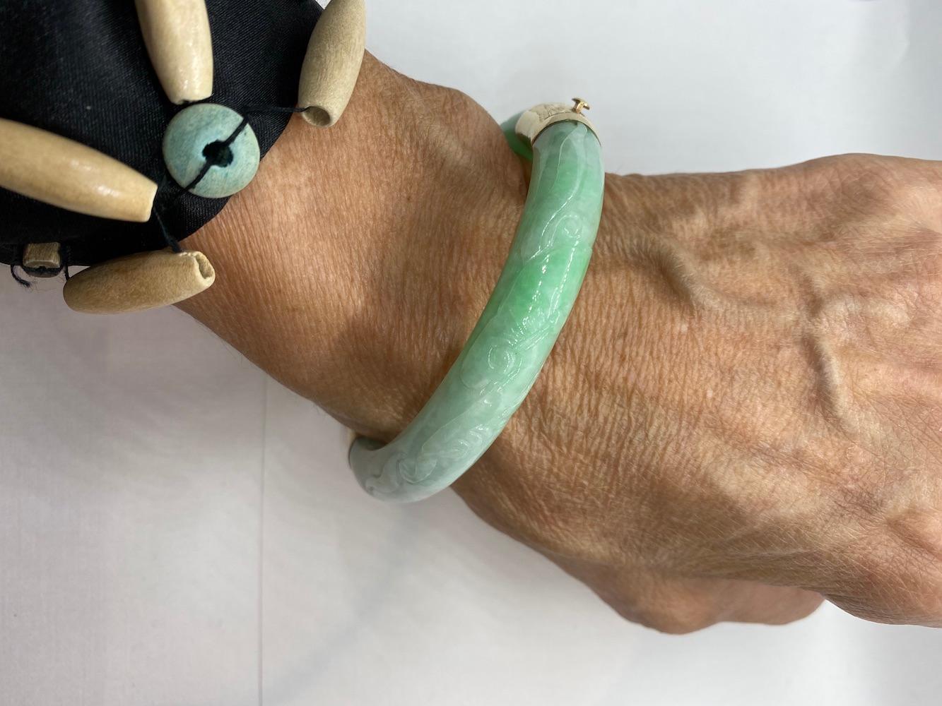 Beautiful, large style bangle Jade Bracelet with carving on top of a 12 mm wide solid Jadeite. 
Circa 1970's from Newport Beach, Ca estate,
14 karat yellow gold large bands of etched, end pieces comprised of heavy clasp-style closure,
Yellow gold