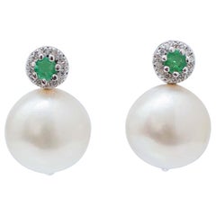 Boucles d
oreilles en or blanc 14 carats, perles blanches de 12 mm, émeraudes, diamants.