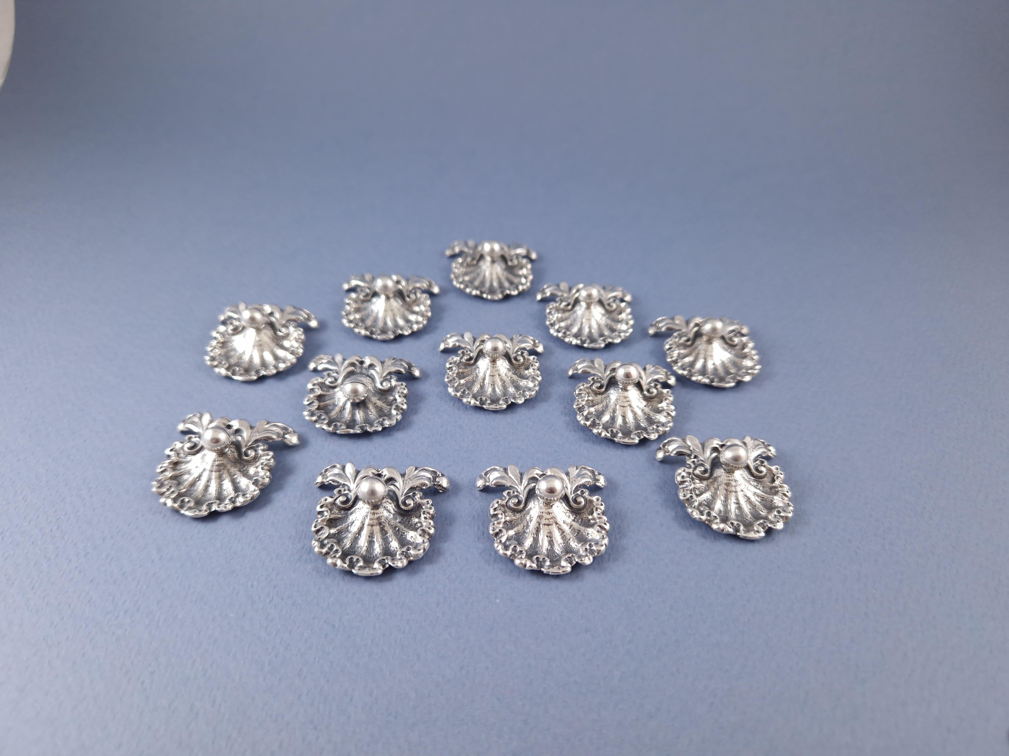 Beautiful set of twelve place cards holders in solid silver 
In the shape of a shell and decorated with foliage 

800 silver hallmark 
Length: 3.3 cm 
Width: 3.4 cm 
Weight: 111 grams
In great condition