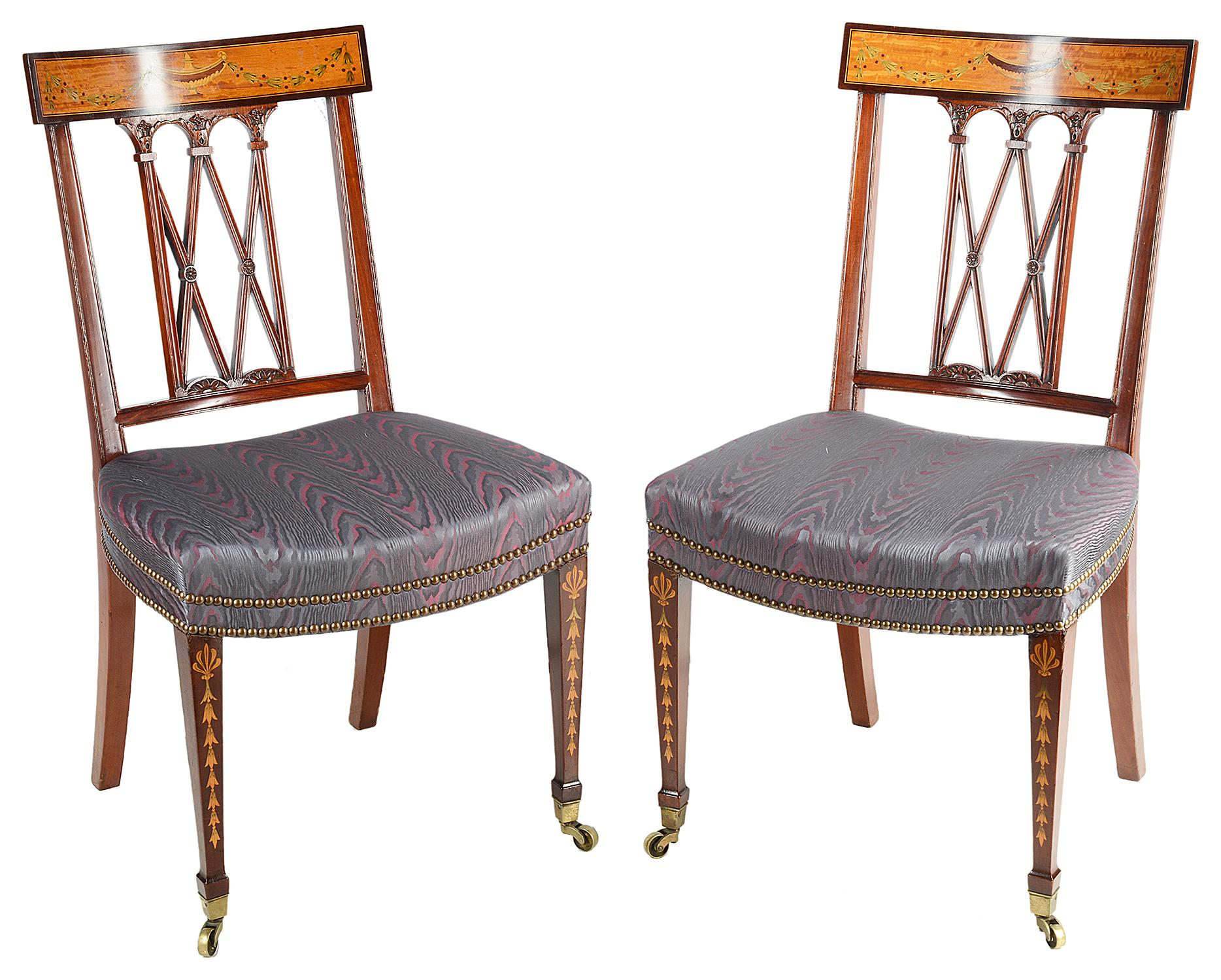 A very good quality set of twelve Sheraton Revival mahogany inlaid dining chairs, each with beautiful marquetry inlaid urns and swags to the satinwood backrests, and carved X-frames. The stuff-over upholstered seats with brass studs, raised on