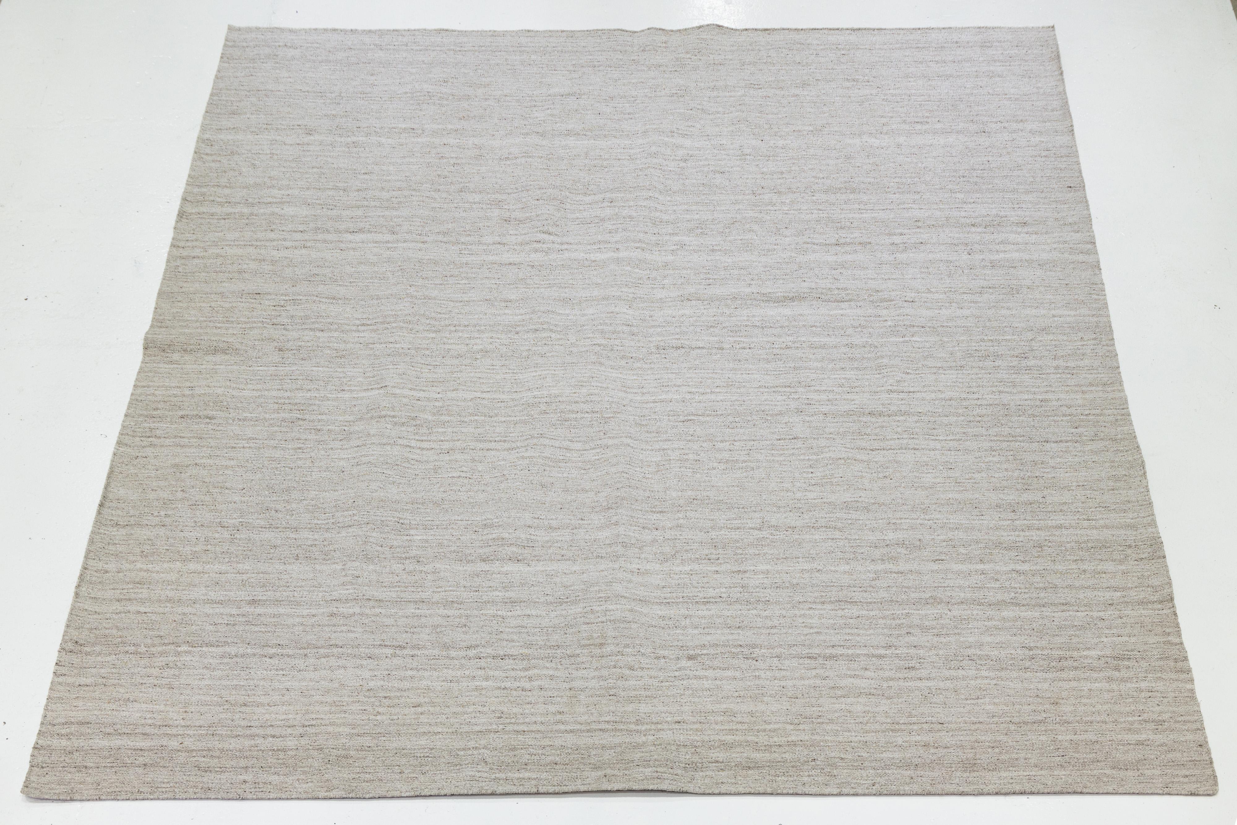 Dieser Teppich zeichnet sich durch ein organisches, modernes Design aus, das durch ein Flachgewebe aus Wolle (Kilim) gekennzeichnet ist. Er zeigt ein geometrisches Muster in Naturleinen- und Elfenbeintönen und ist damit eine stilvolle Ergänzung für
