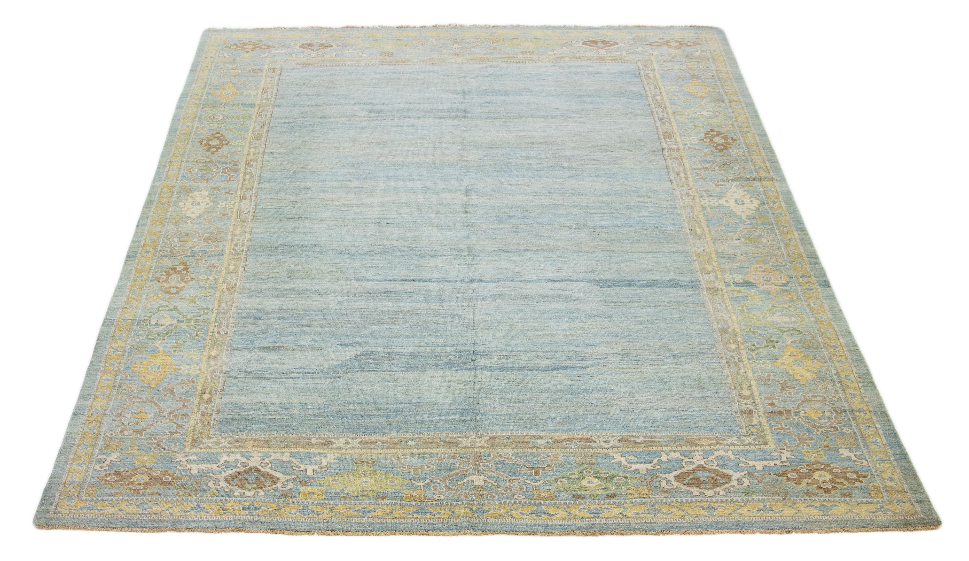 Dieser handgeknüpfte Wollteppich zeigt einen hellblauen Hintergrund mit gelben und beigen Akzenten in einem gerahmten Muster.

Dieser Teppich misst 12'3'' x 15'3