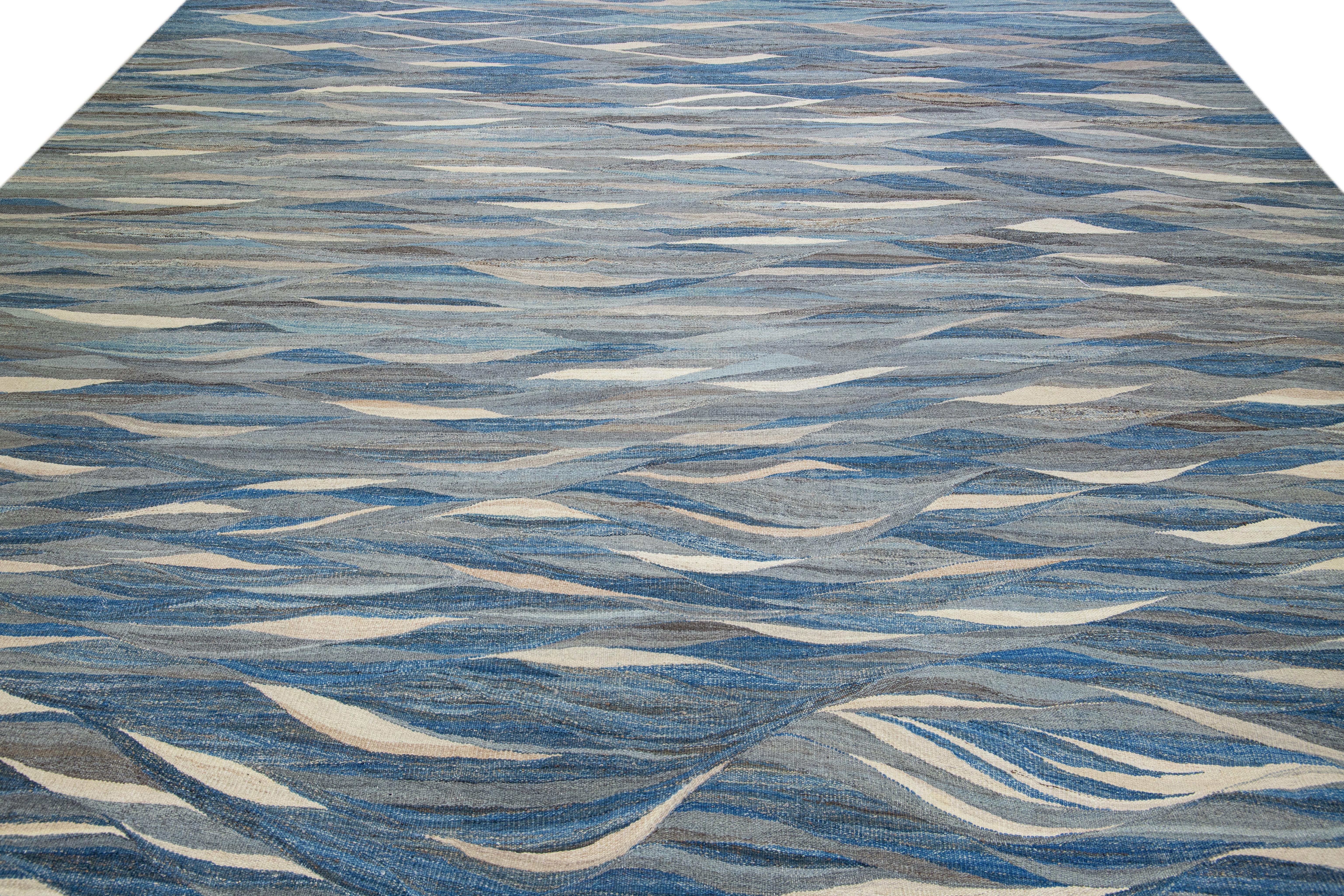 Beautiful modern flat-weave Kilim handmade wool rug featuring a blue field. This Kilim rug showcases earthy tones in a stunning abstract expressionist design. 

The dimensions of this rug are 12' x 14'9