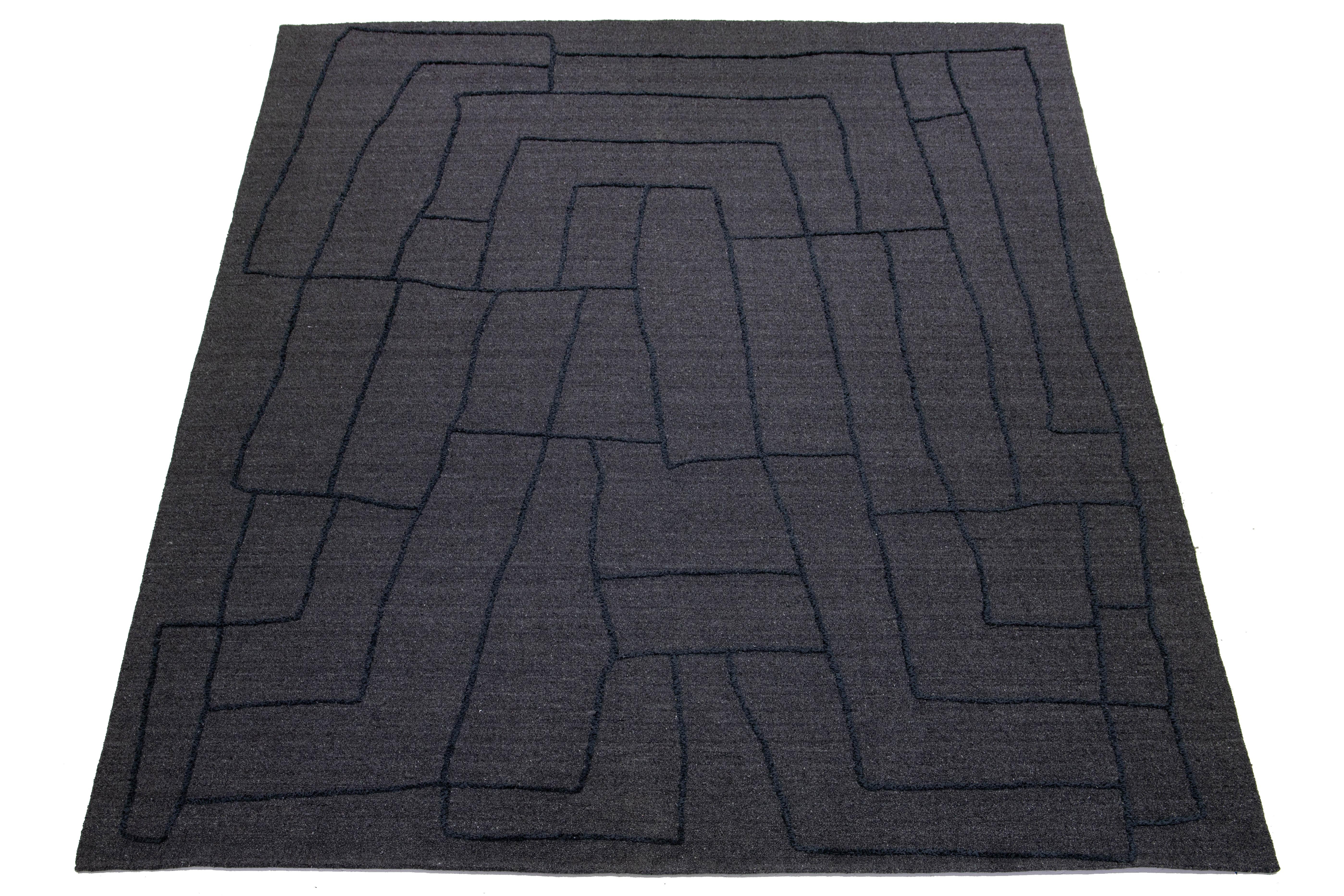 This exquisitely designed modern wool rug is bound to captivate attention. Its sophisticated gray background provides the perfect canvas for the intricate abstract pattern in blue hues. This striking visual contrast infuses depth and personality