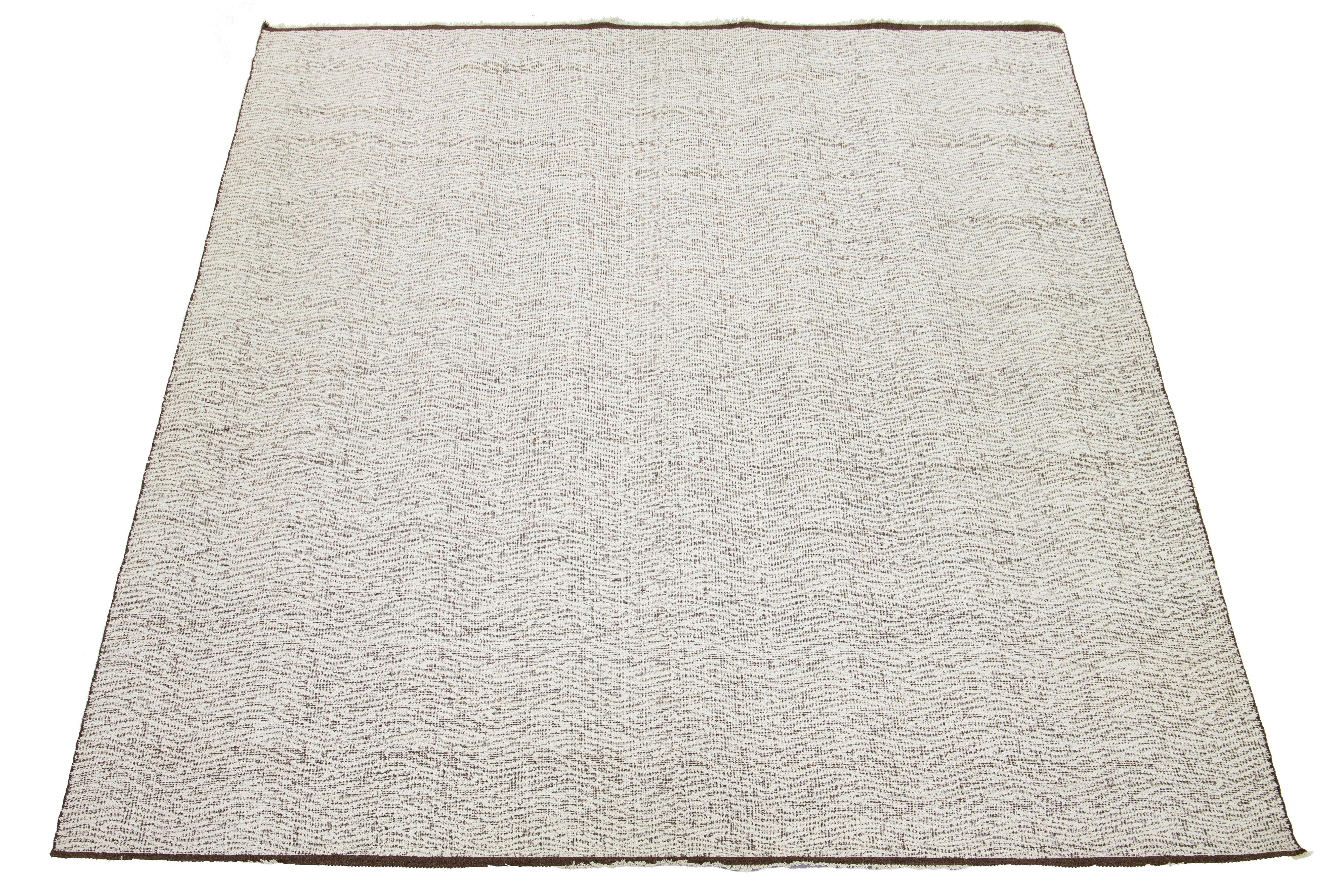 Questo tappeto è caratterizzato da un design organico moderno in lana Kilim a trama piatta con un motivo di base marrone e avorio. 

Questo tappeto misura 11'11